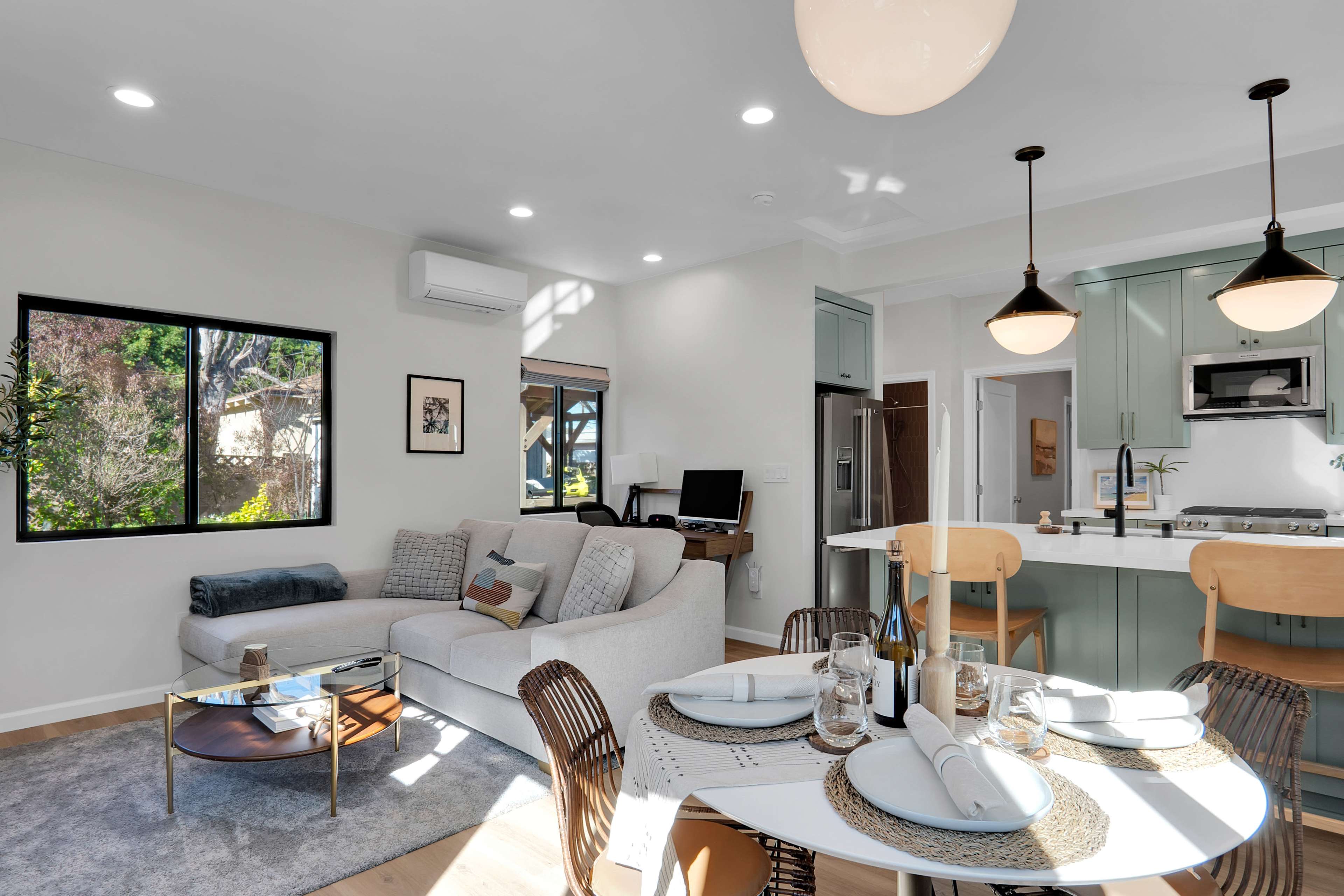 A modern living space features a light-colored couch, a dining table set for four, and a kitchen with green cabinetry.