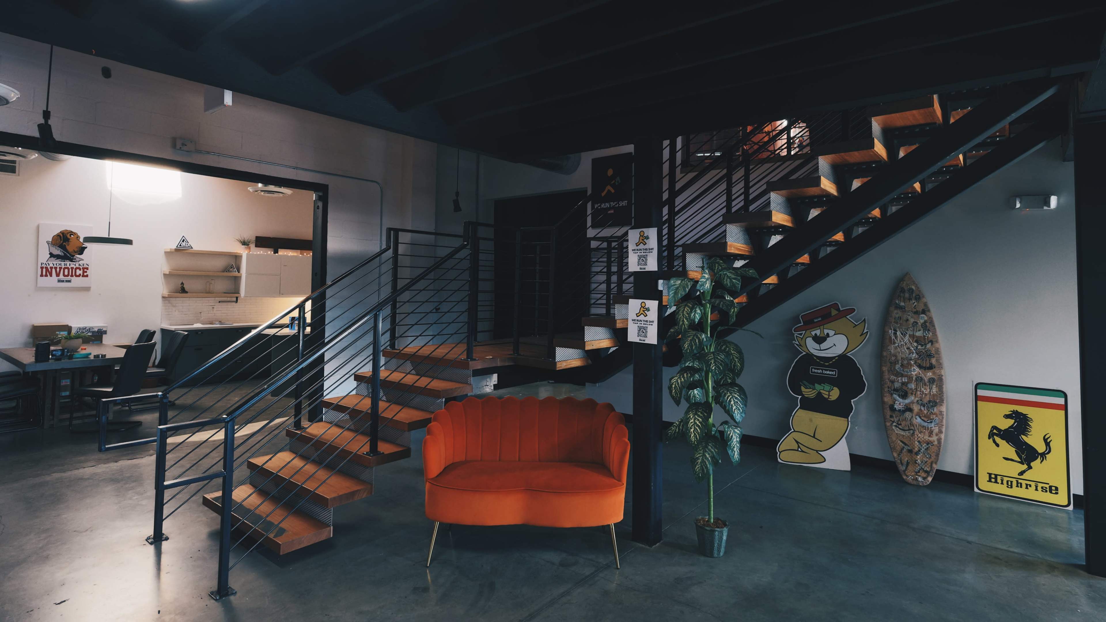 A modern office space with a curved orange sofa, a staircase, and wall decorations, including a cartoon character and a surfboard.