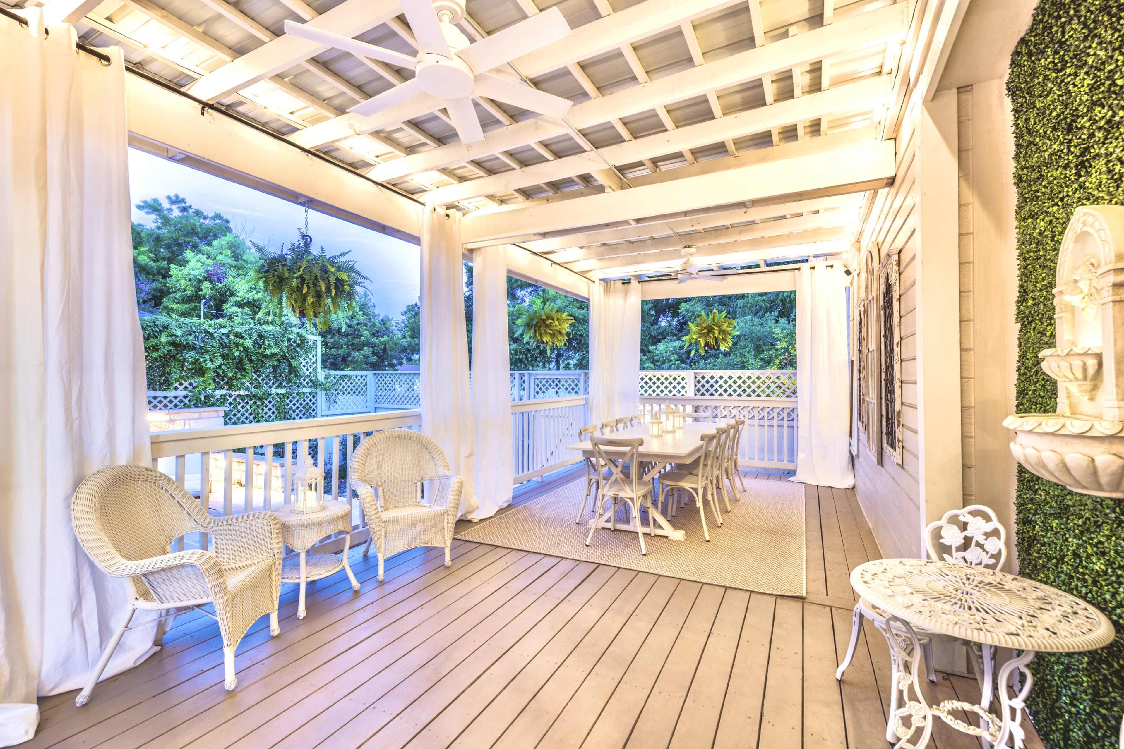 The image shows a covered patio with a table set for dining, surrounded by white curtains and greenery.