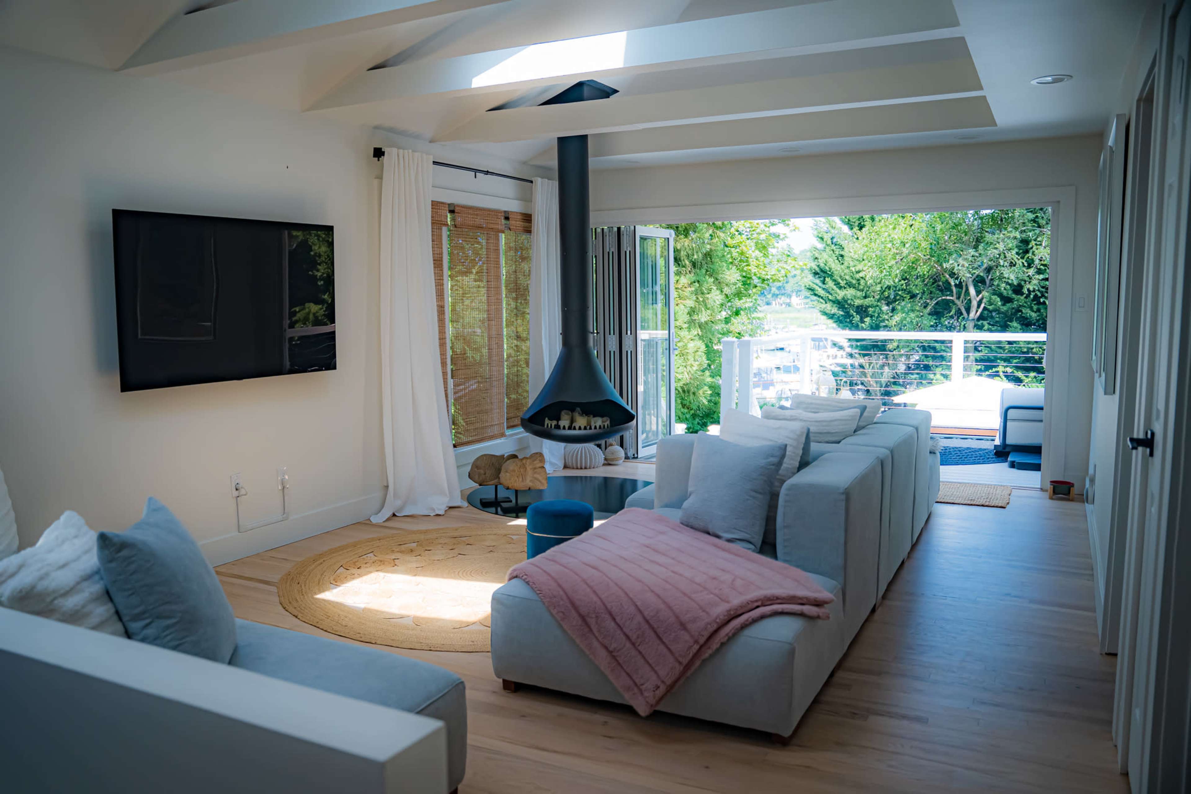 A bright living room features a large sectional sofa, a modern fireplace, and large windows overlooking greenery.