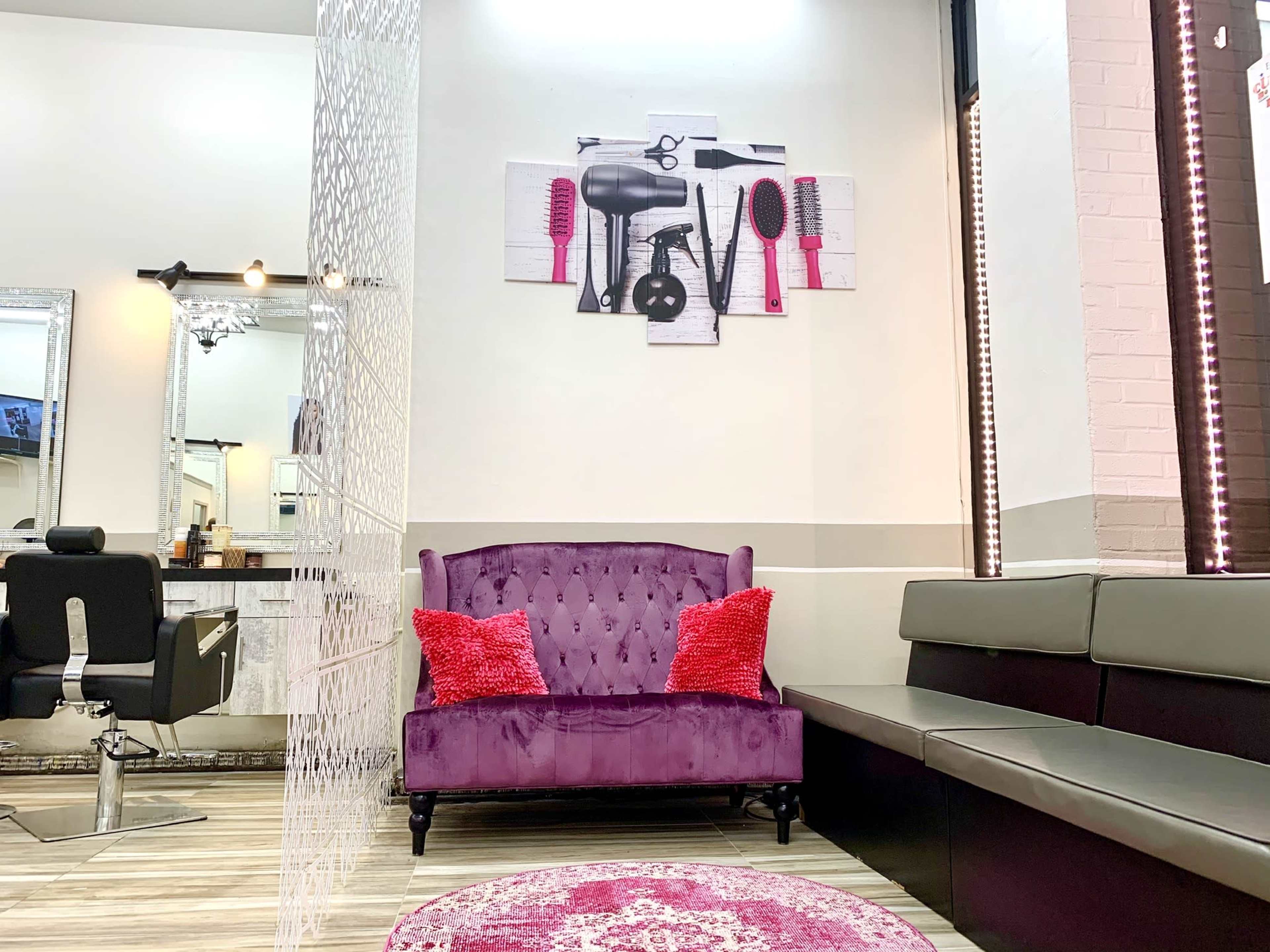 A stylish salon interior featuring a purple velvet sofa with decorative pillows, a circular rug, and a wall adorned with various hair styling tools.