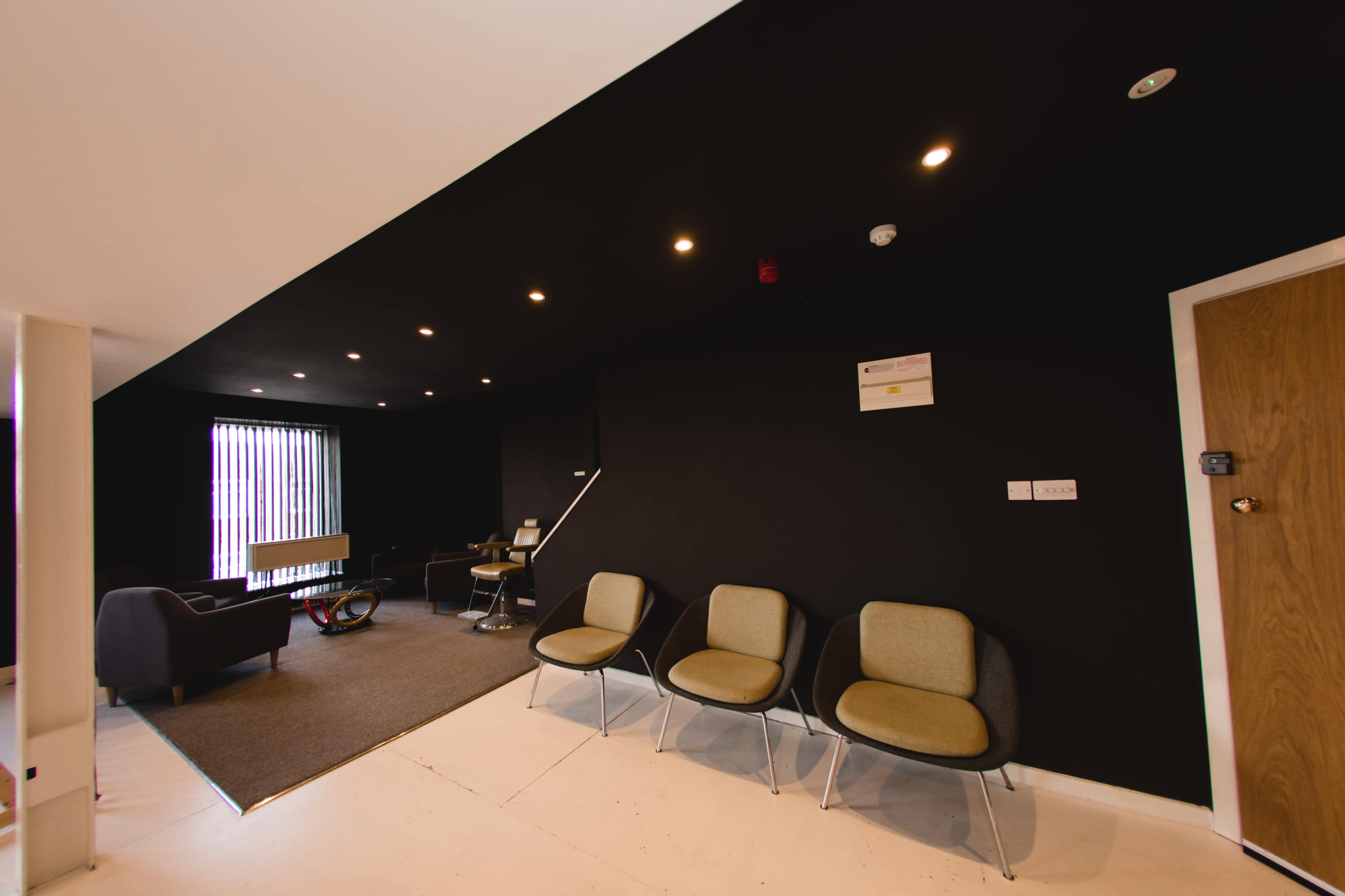 A modern interior space with a black wall, three gray chairs, and a small table in a lounge area.