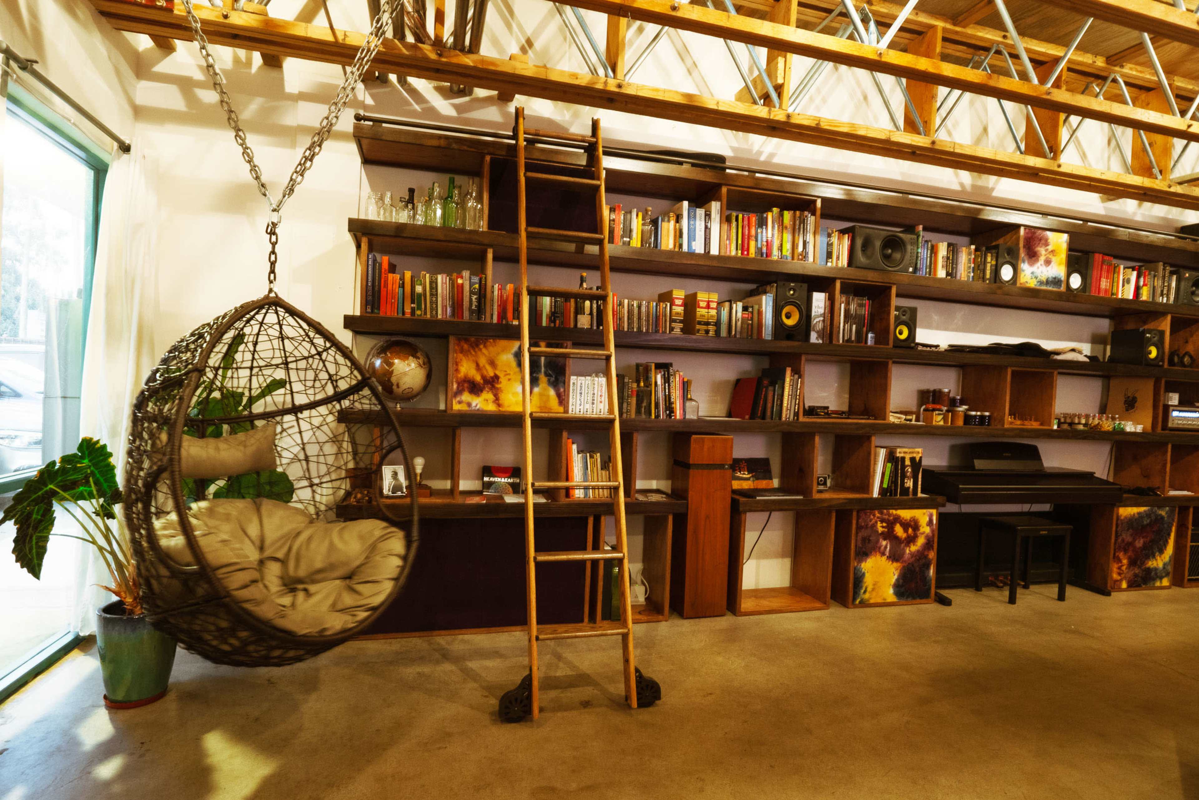 A spacious interior with a hanging chair, a wooden ladder leading to a shelf filled with books and decorative items, and a minimalist black desk.