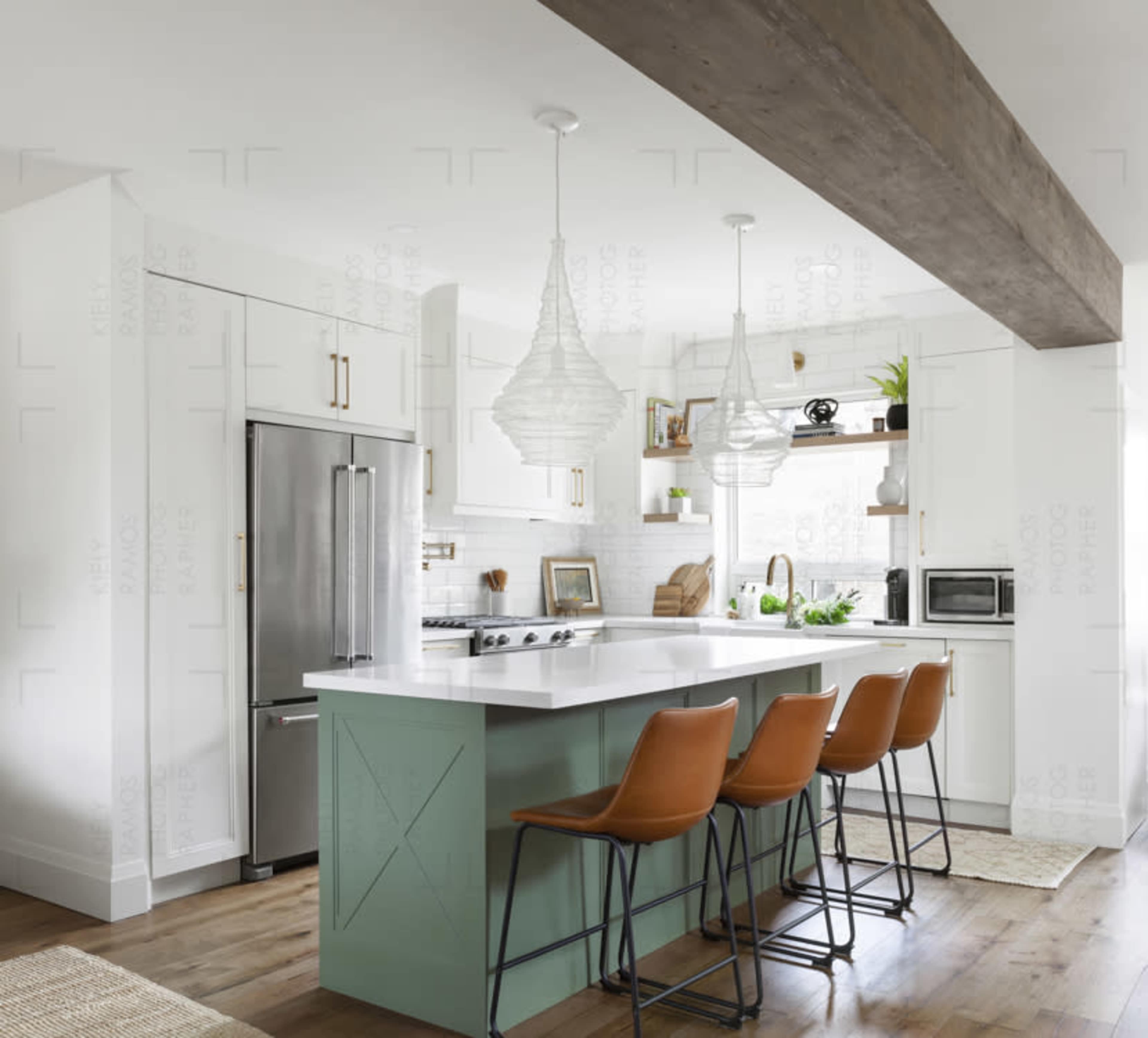 A modern kitchen features a large island with green cabinetry and three brown bar stools, flanked by pendant lights and stainless steel appliances.