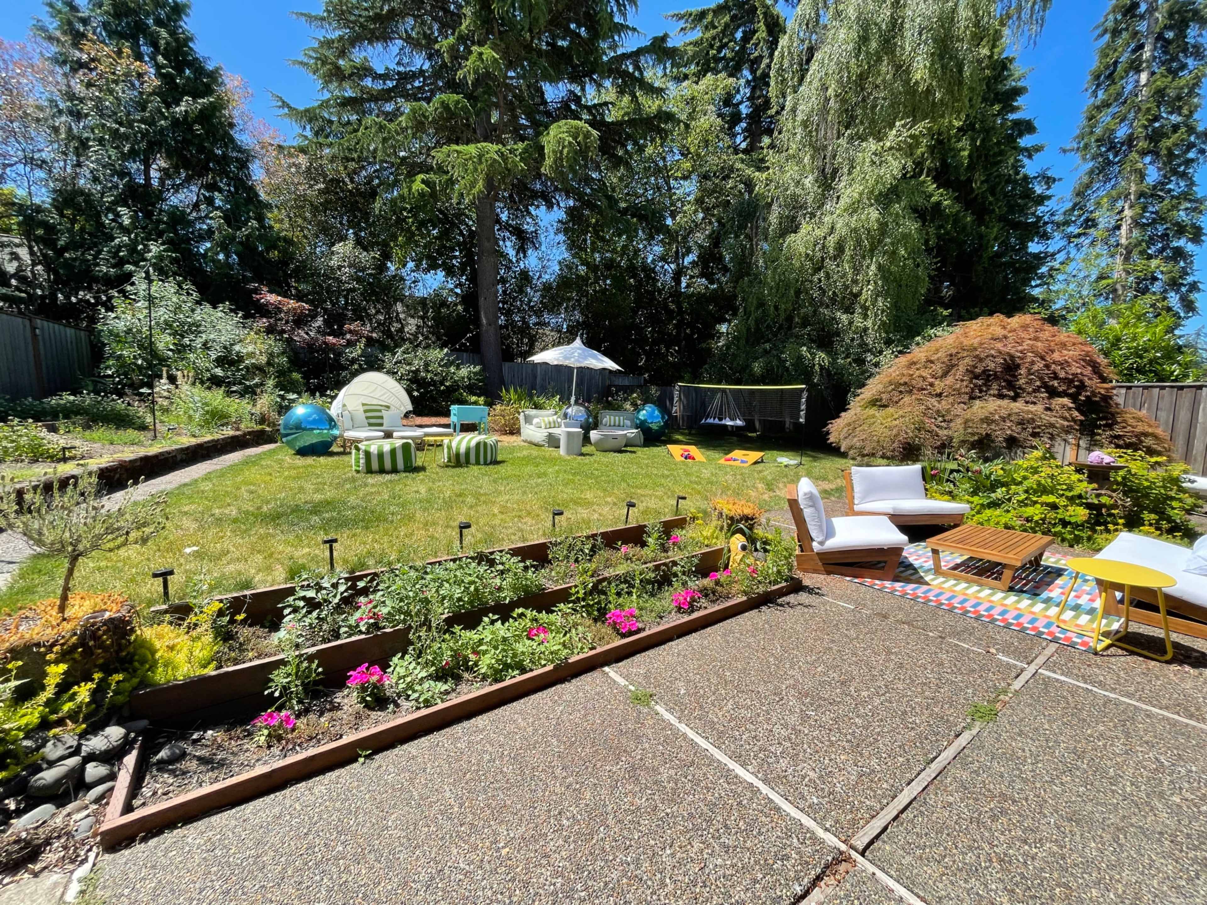 The image shows a well-maintained backyard with a grassy area, lounge furniture, colorful decorations, and various outdoor amenities.