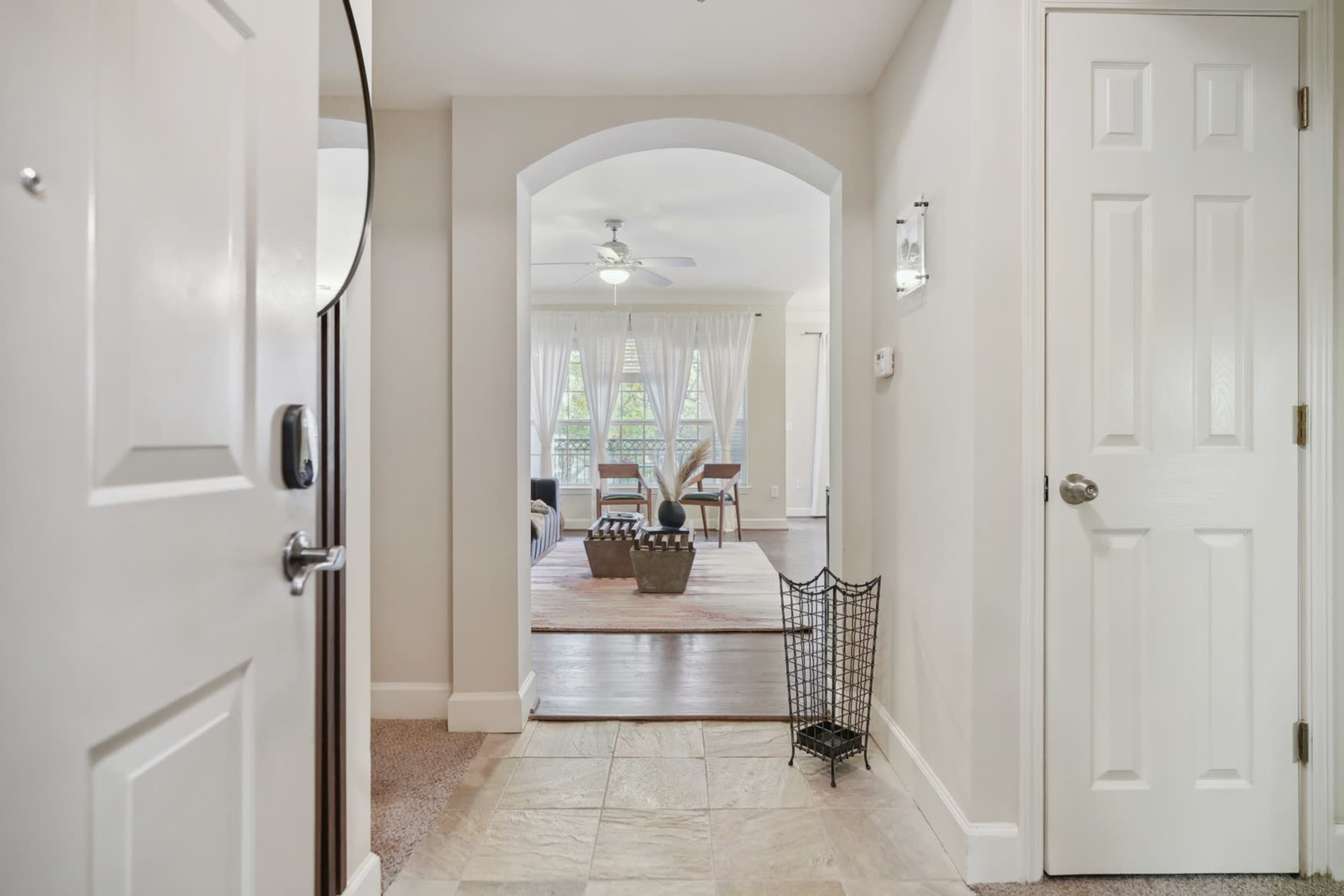 A hallway leading to a bright living area with a dining table and large windows, framed by an arched doorway.