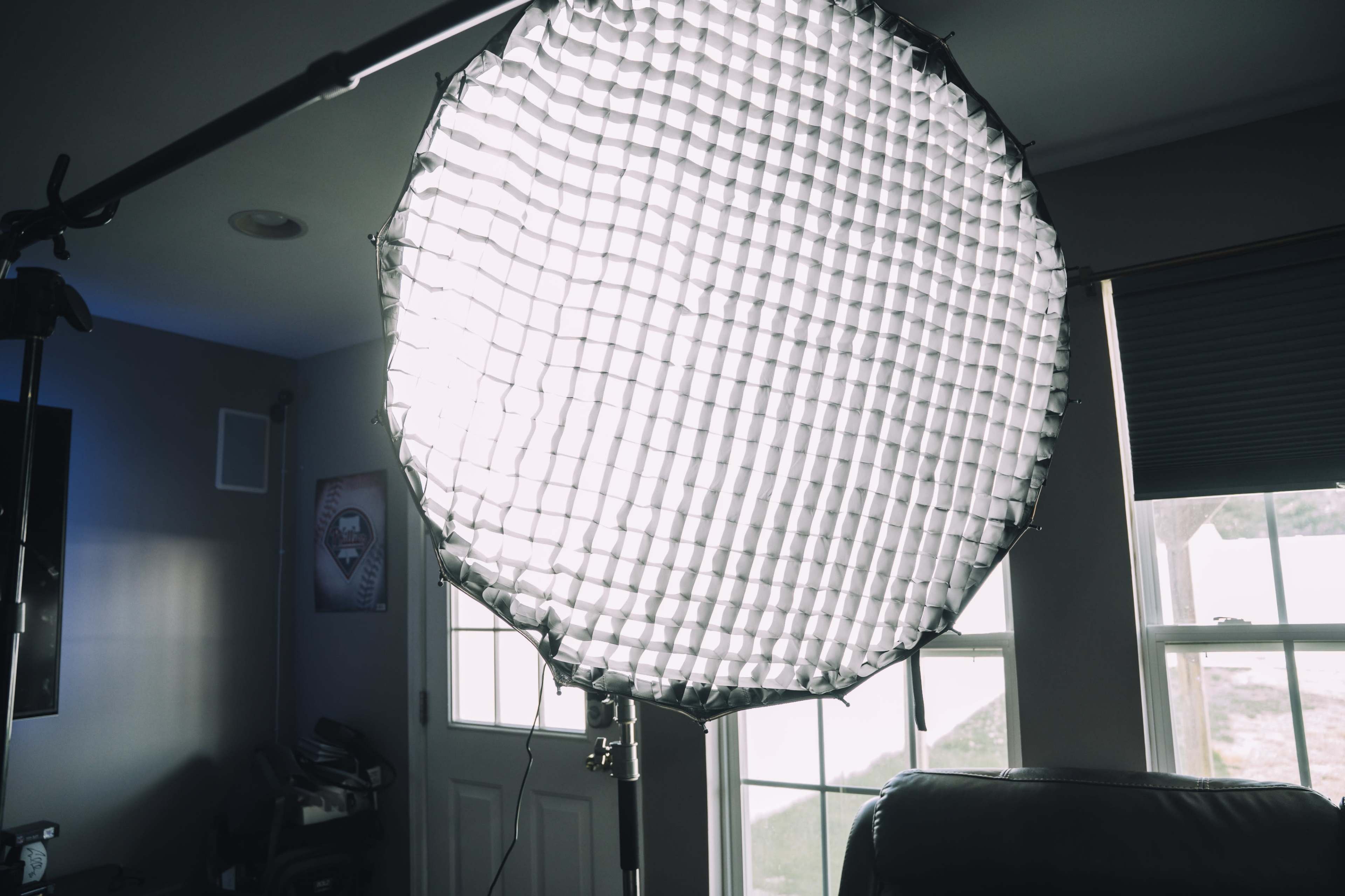 A large softbox with a grid is mounted on a stand in a room near a door and windows.