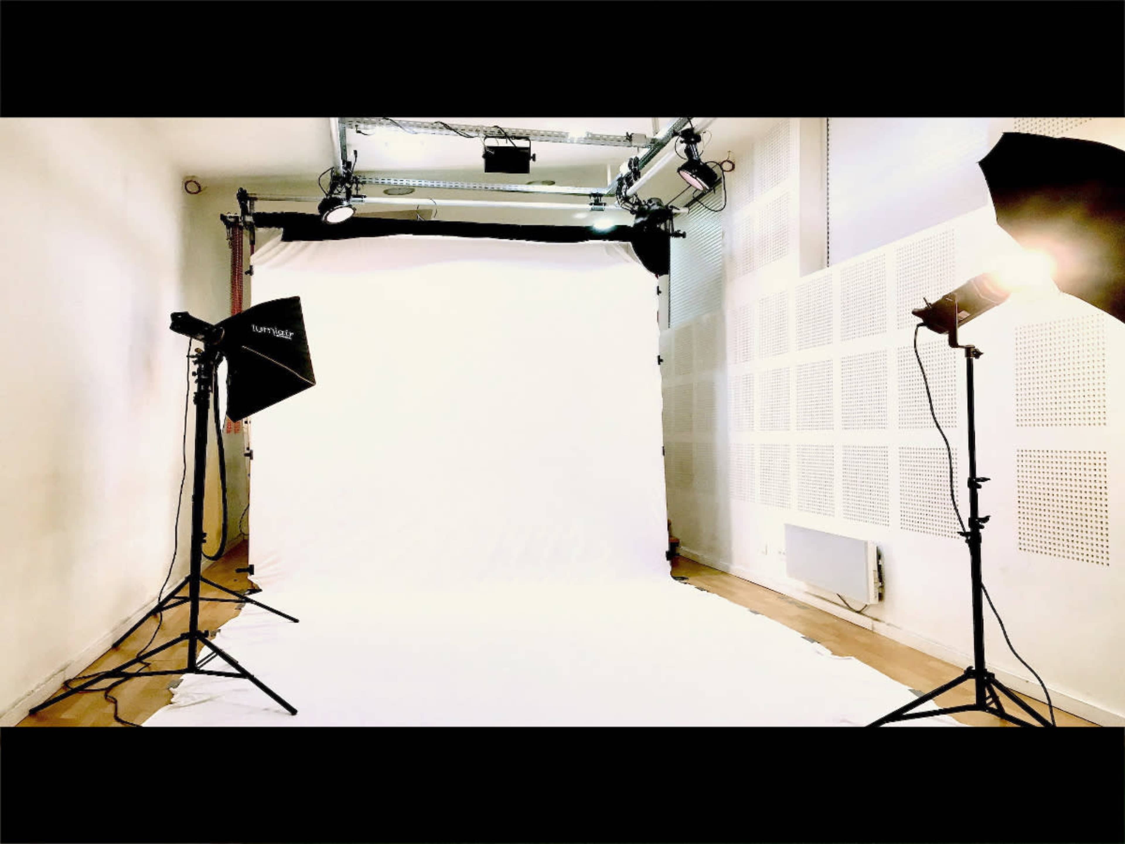 A photography studio with a white backdrop and lighting equipment positioned around it.