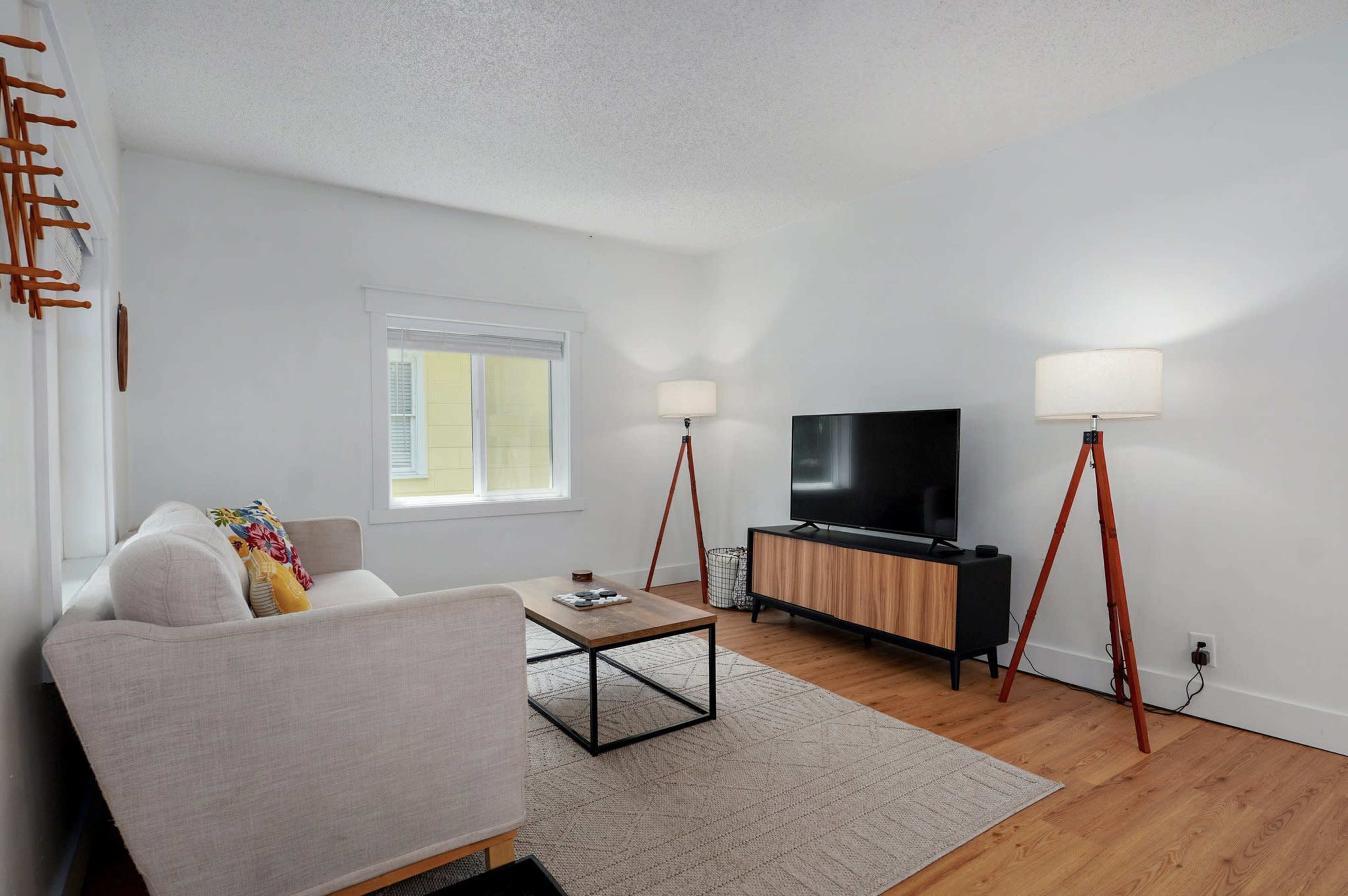The image shows a modern living room with a beige couch, a wooden coffee table, a TV on a stand, and two floor lamps.
