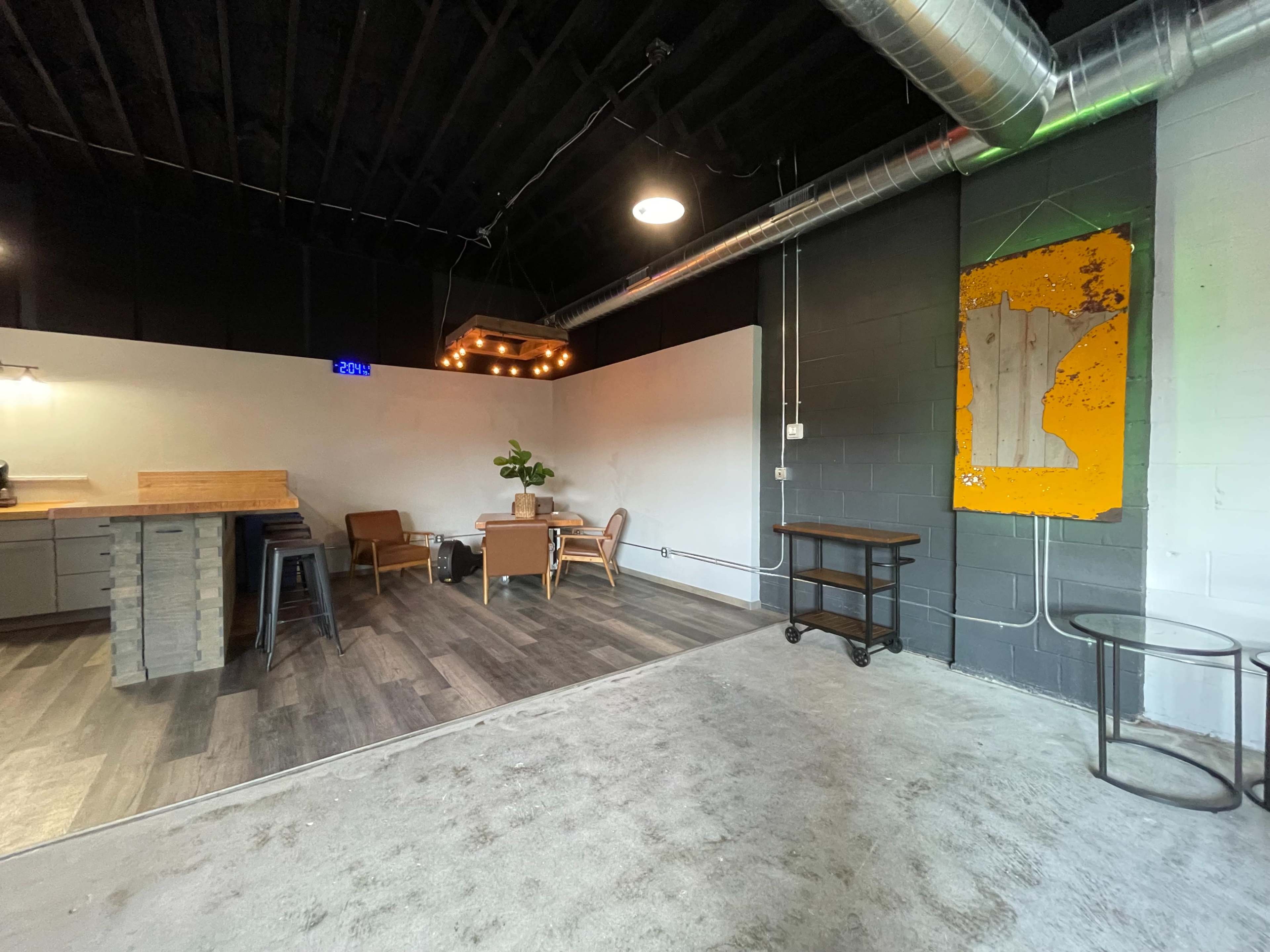 A contemporary open space featuring a kitchen area with a wooden bar, seating arrangements, and a wall with an abstract artwork.