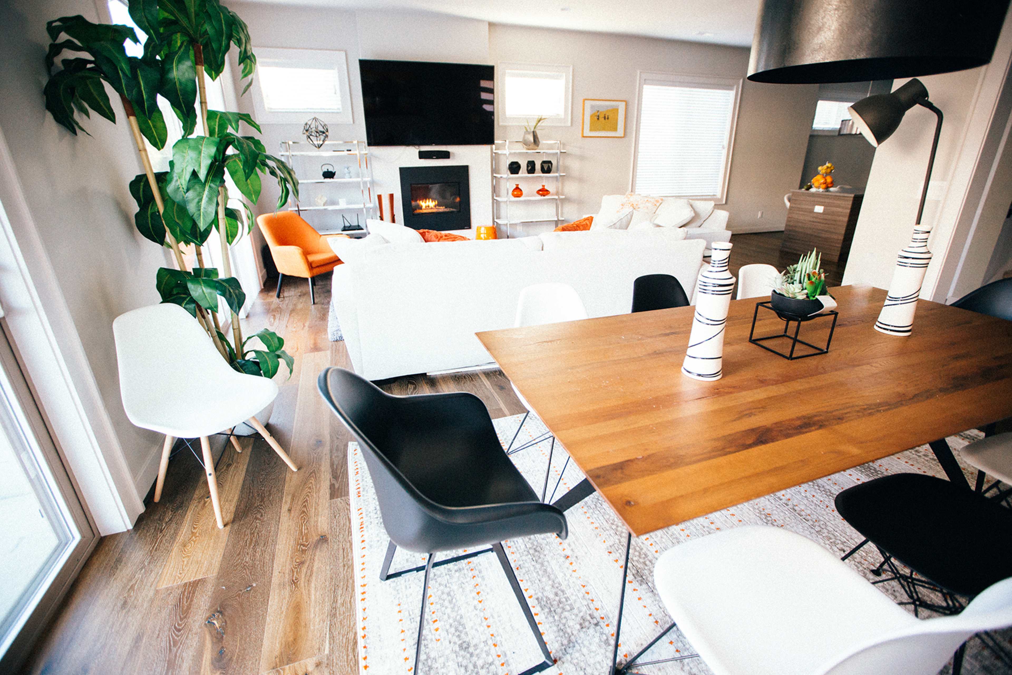 A modern living space with a dining table surrounded by various chairs, a white sofa in the background, and a large television mounted on the wall.