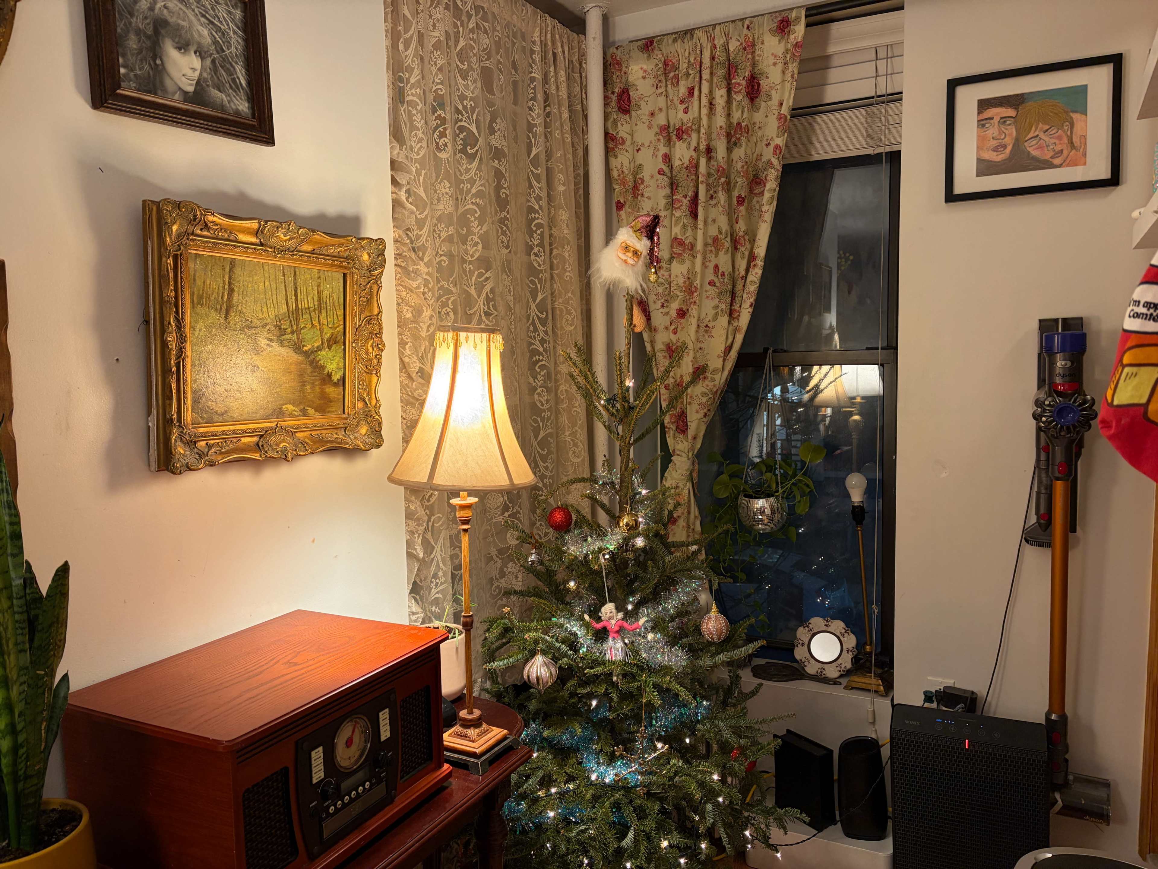A decorated Christmas tree stands in a living room corner next to a vintage radio, a lamp, and a window draped with patterned curtains.