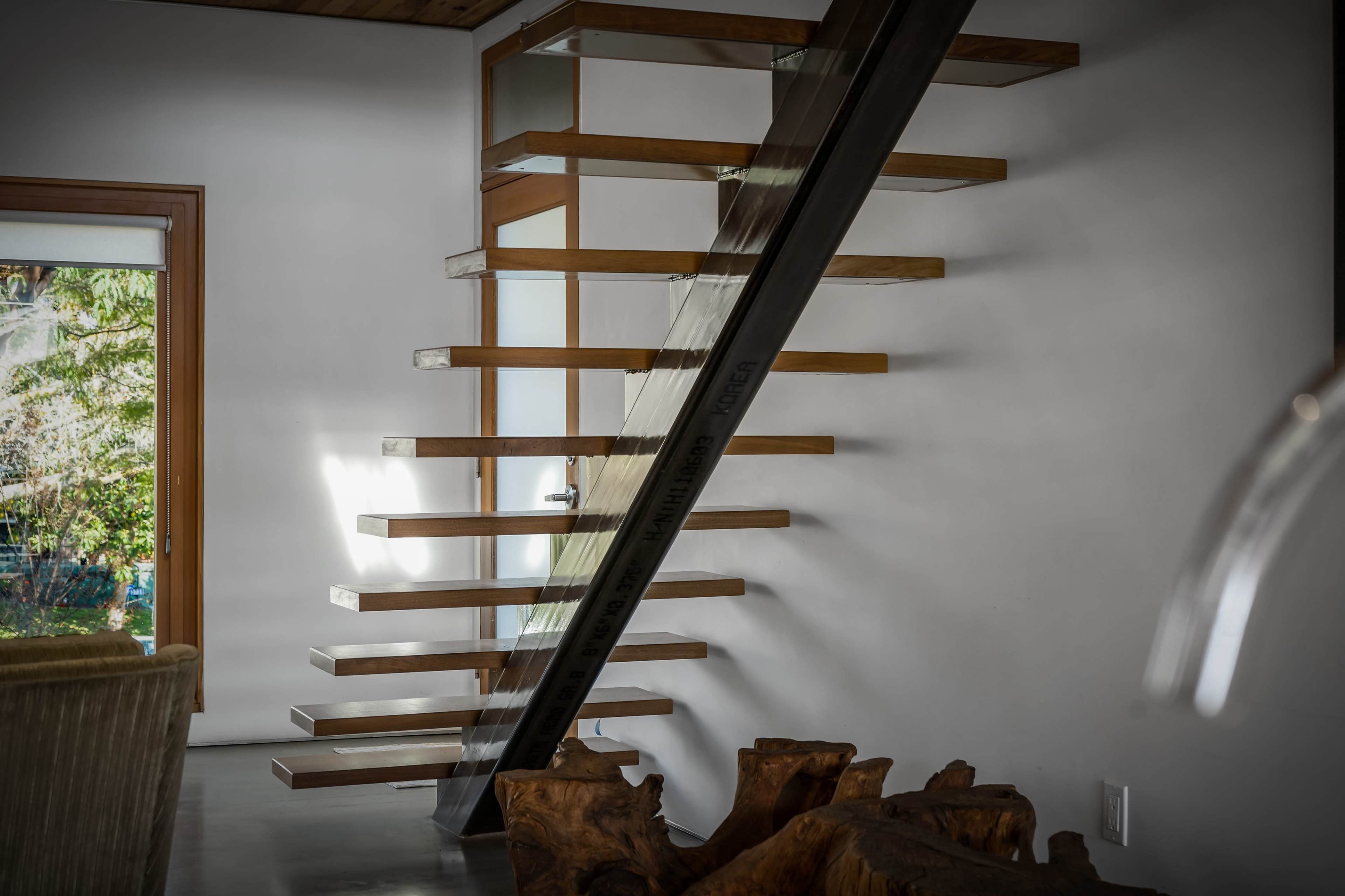 A modern staircase with wooden treads and a metal support beam leads to an upper level in a minimalist interior space.