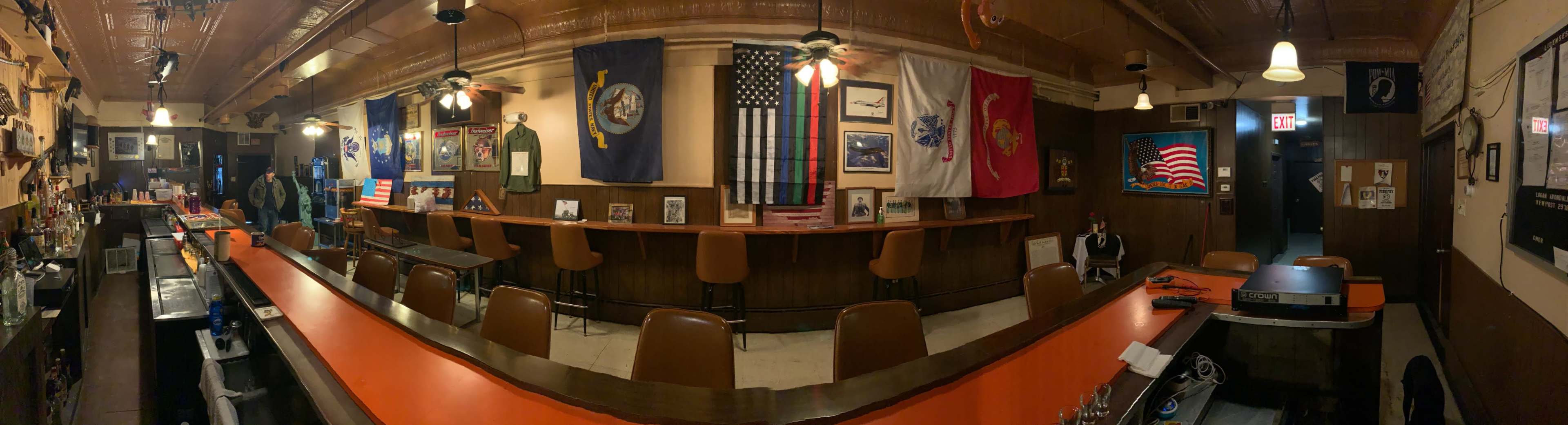 A diner-style bar with a long counter lined with brown stools, decorated with military flags and memorabilia on the walls.