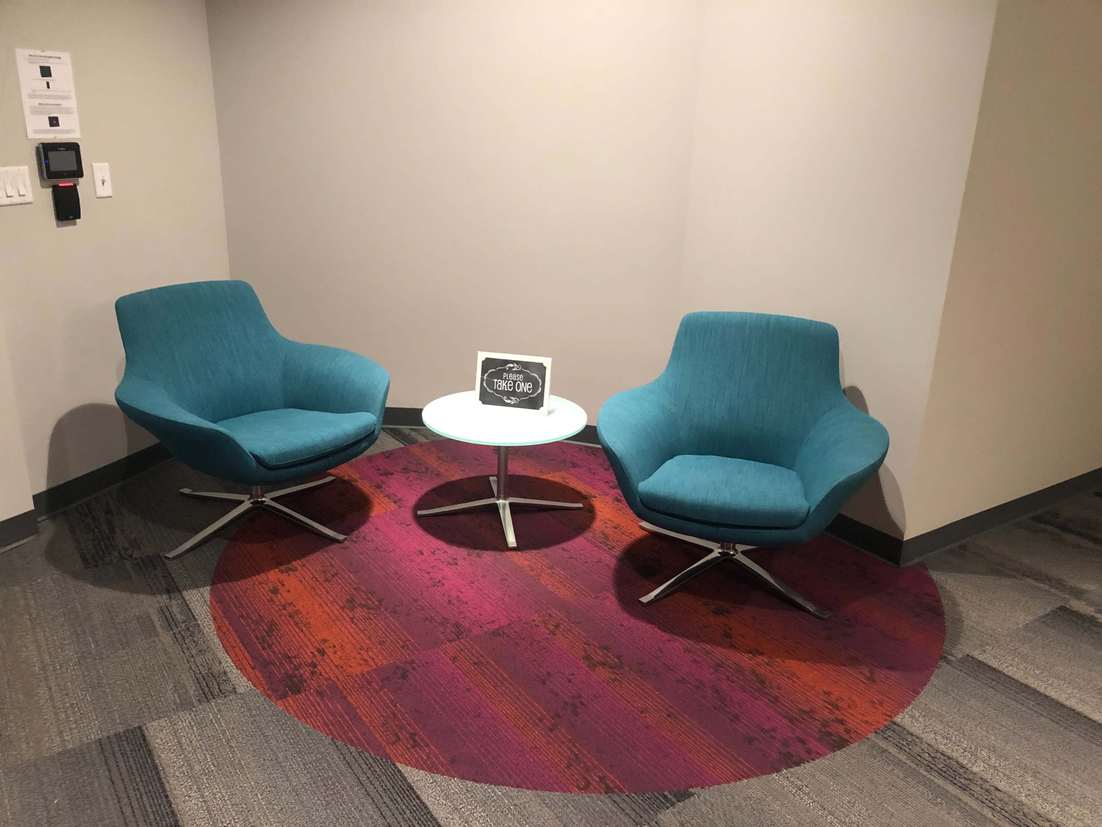 Two teal chairs are positioned opposite each other around a circular table on a patterned rug in a modern indoor space.