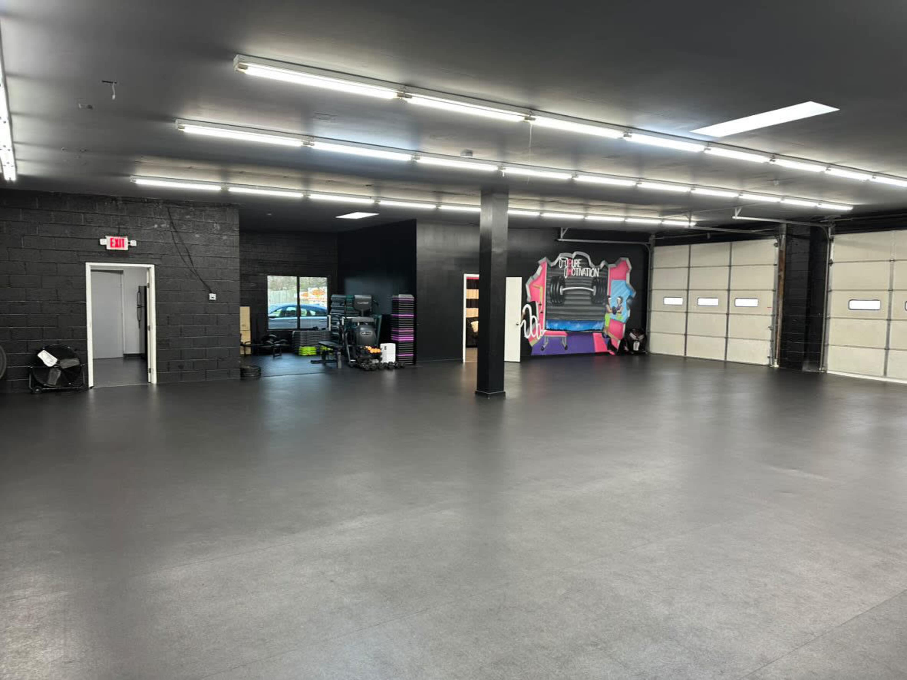 The image shows a spacious, empty room with polished black flooring and large garage doors on one side.