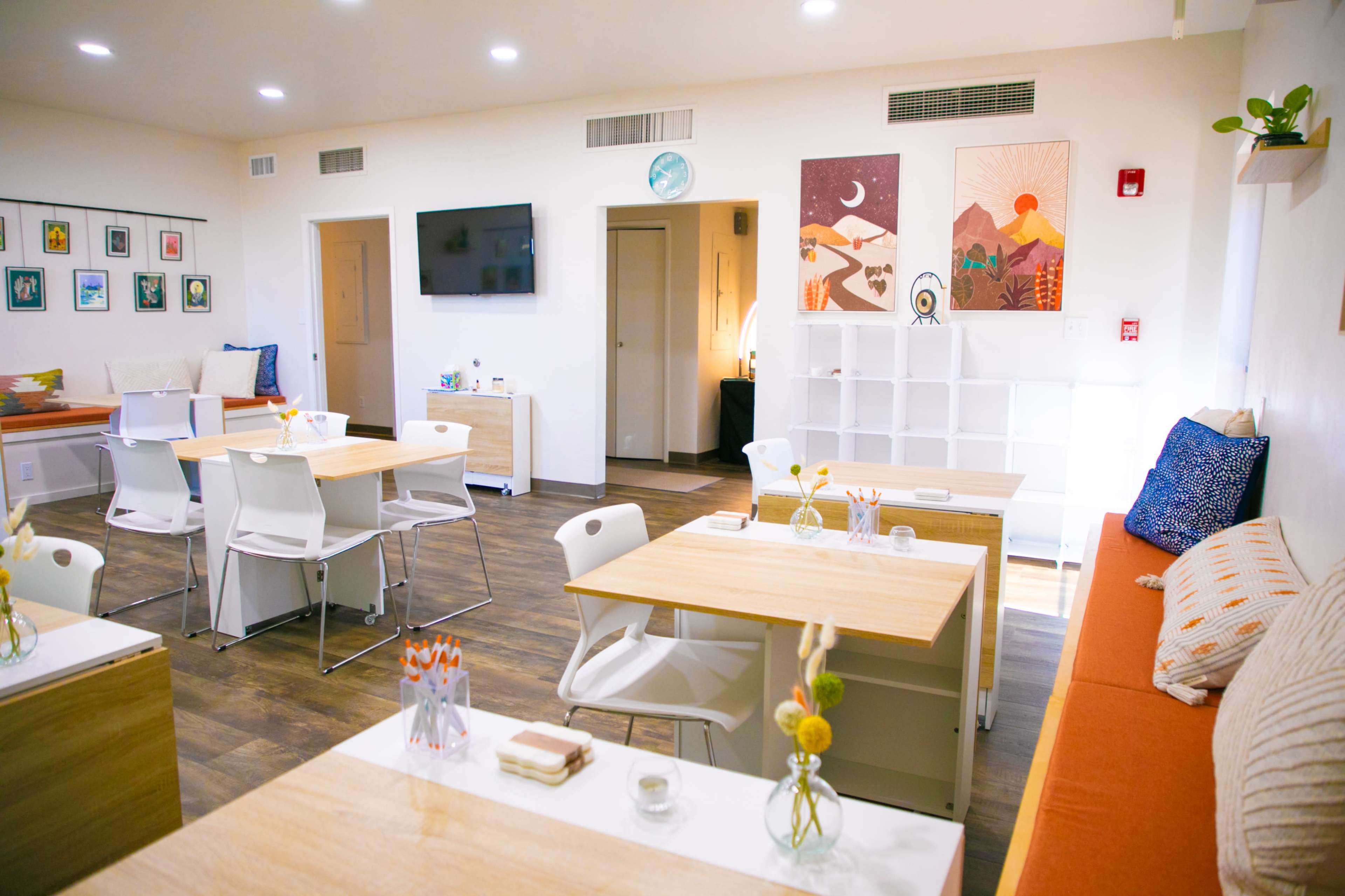 A bright, inviting workspace with white tables, chairs, and a cozy seating area, adorned with artwork on the walls.