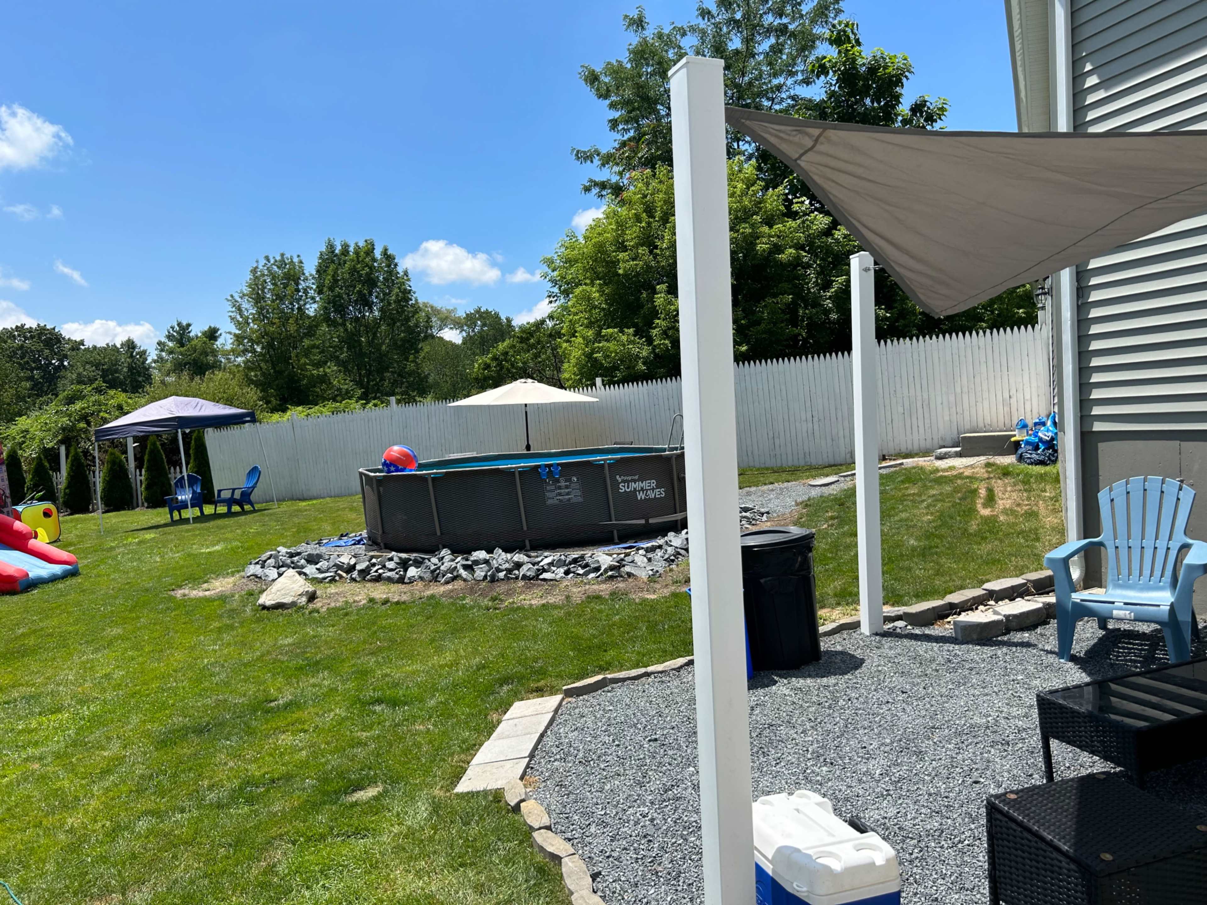 A backyard with a pool, lounge chairs, a gazebo, and shade sails.