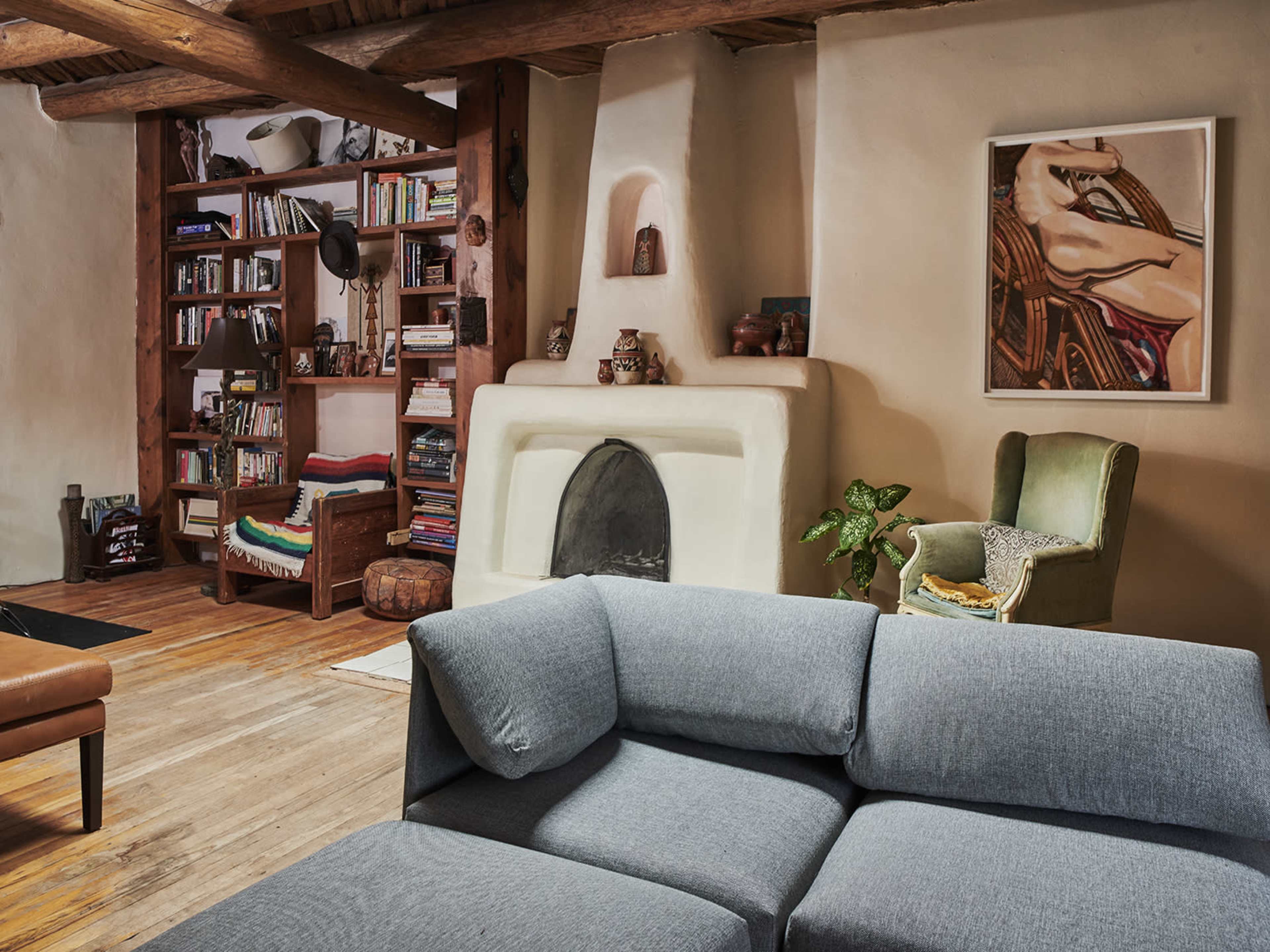 A cozy living room with a gray sectional sofa, a wooden coffee table, shelves filled with books, and a fireplace built into a beige wall.