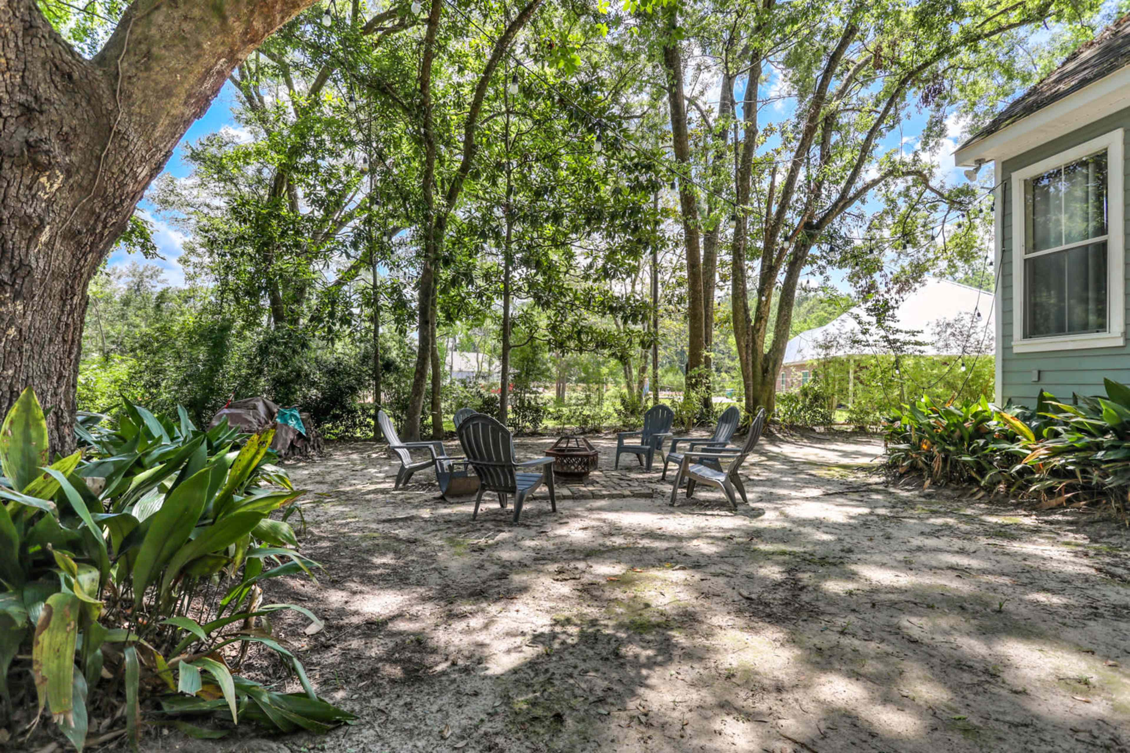 A clearing surrounded by trees features several outdoor chairs arranged around a fire pit.