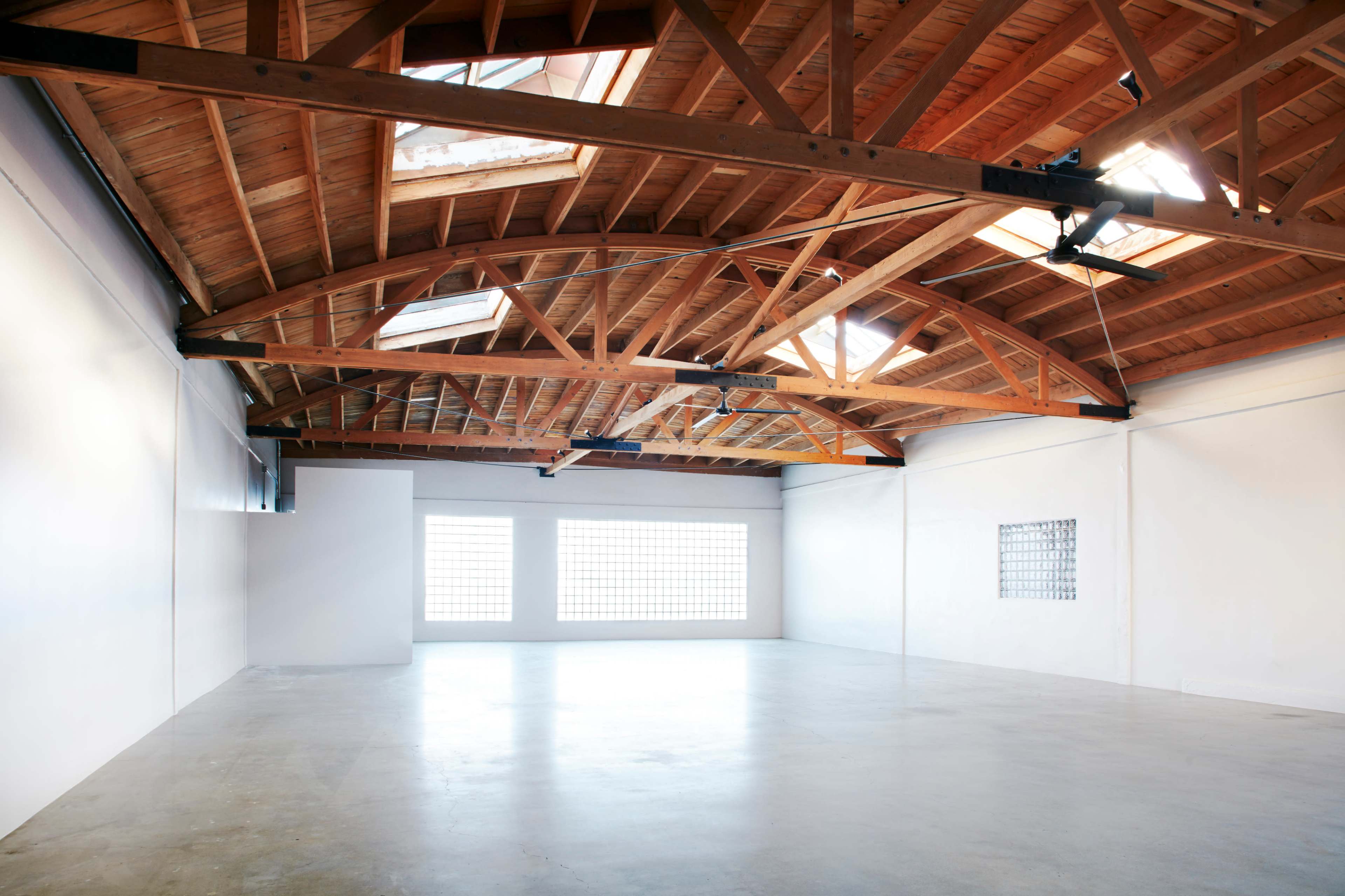 A spacious, empty room with high wooden ceilings and large windows allowing natural light to enter.