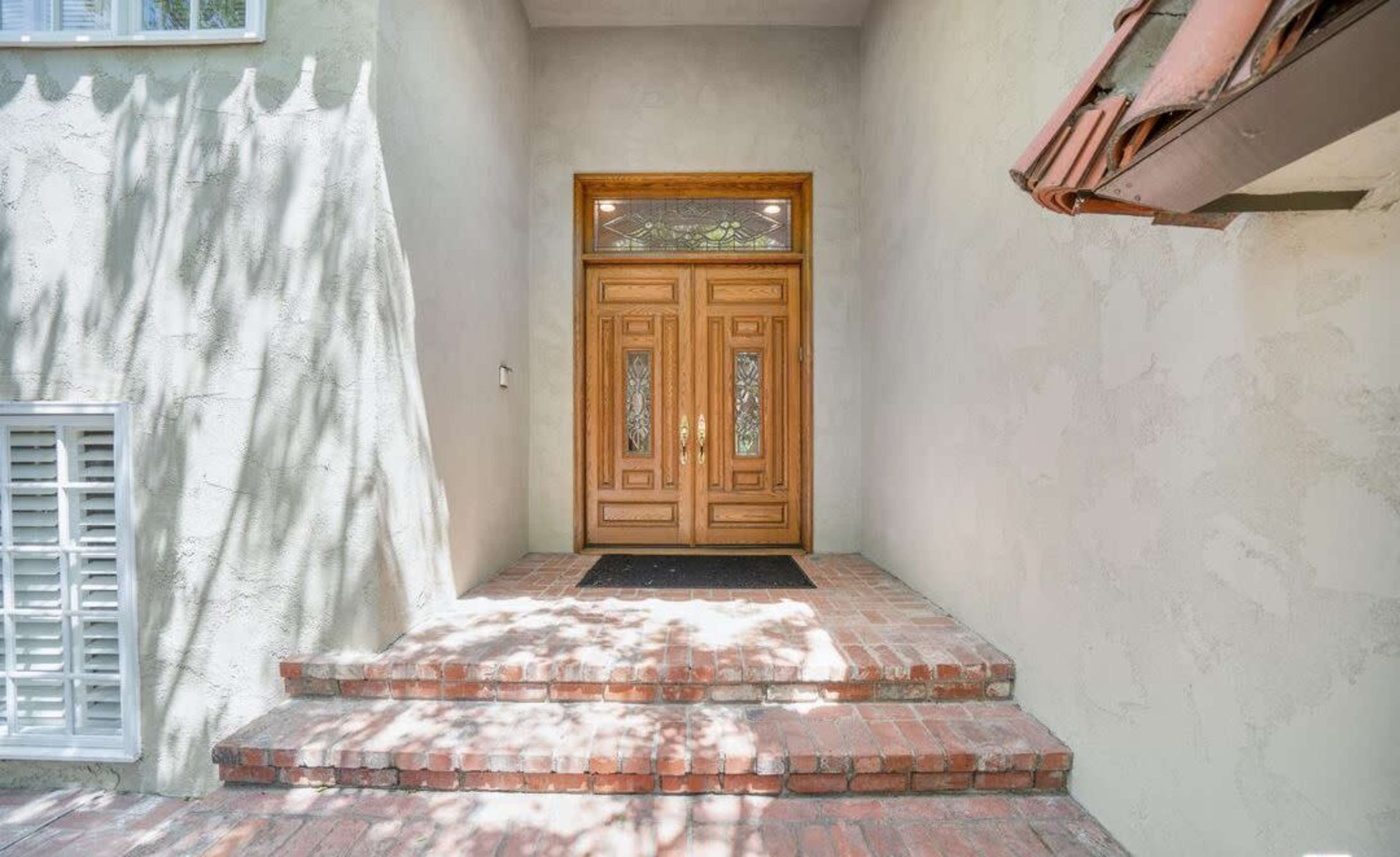 The image shows a front entrance with a wooden double door, flanked by windows, leading up a set of brick steps.
