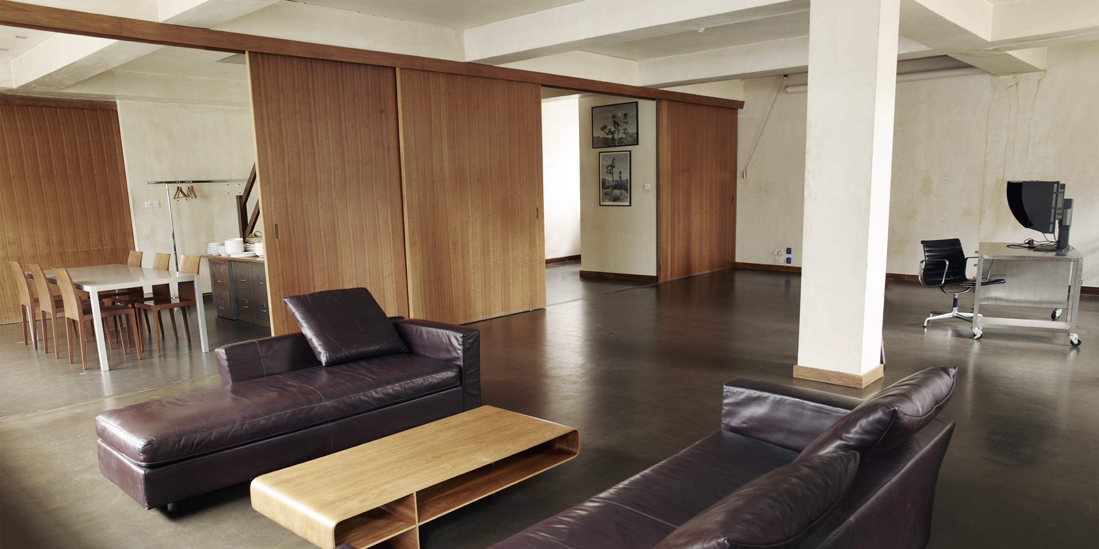 A modern, open-concept living space with leather sofas, a wooden coffee table, and sliding wood-panel doors leading to another room.