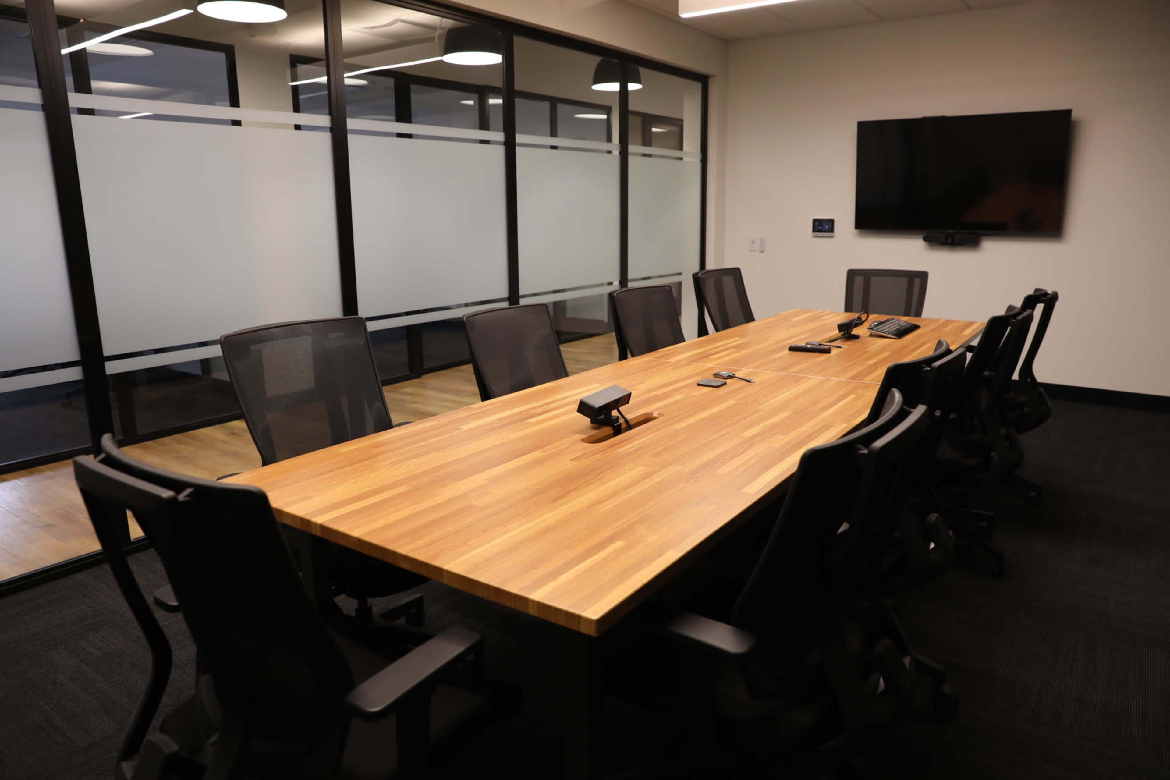 A large conference room features a wooden table surrounded by ergonomic chairs and a wall-mounted television.