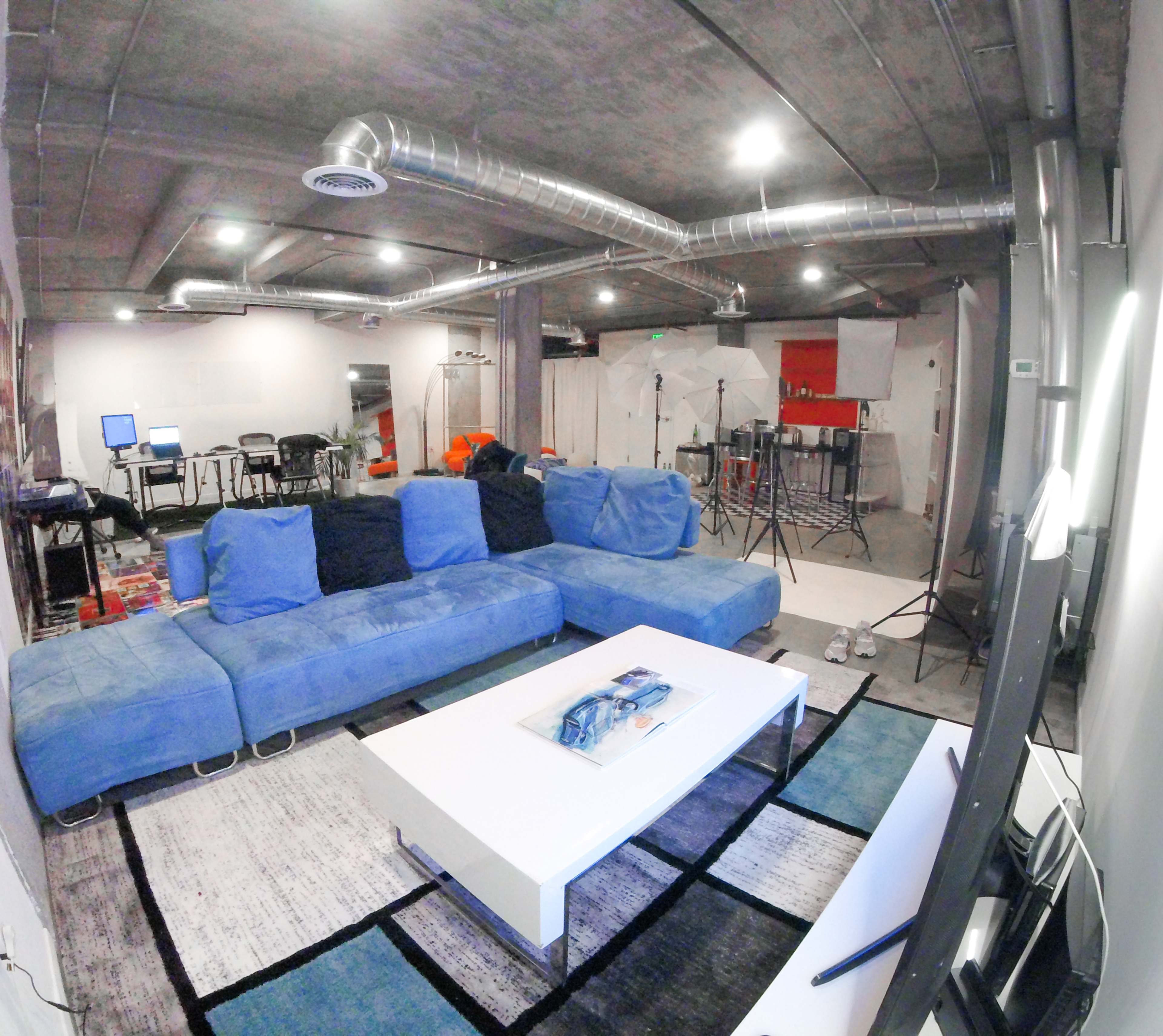 A spacious modern living area with a large blue sectional sofa, a white coffee table, and various filming equipment set up in the background.