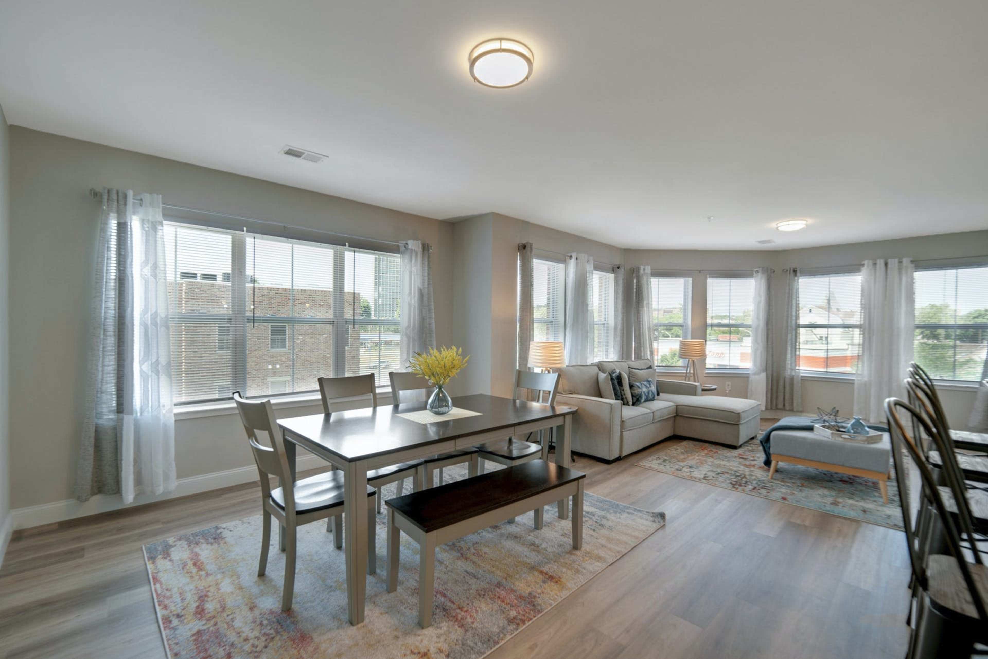 A modern living space features a dining area with a table and chairs, adjacent to a cozy seating arrangement with large windows allowing natural light.