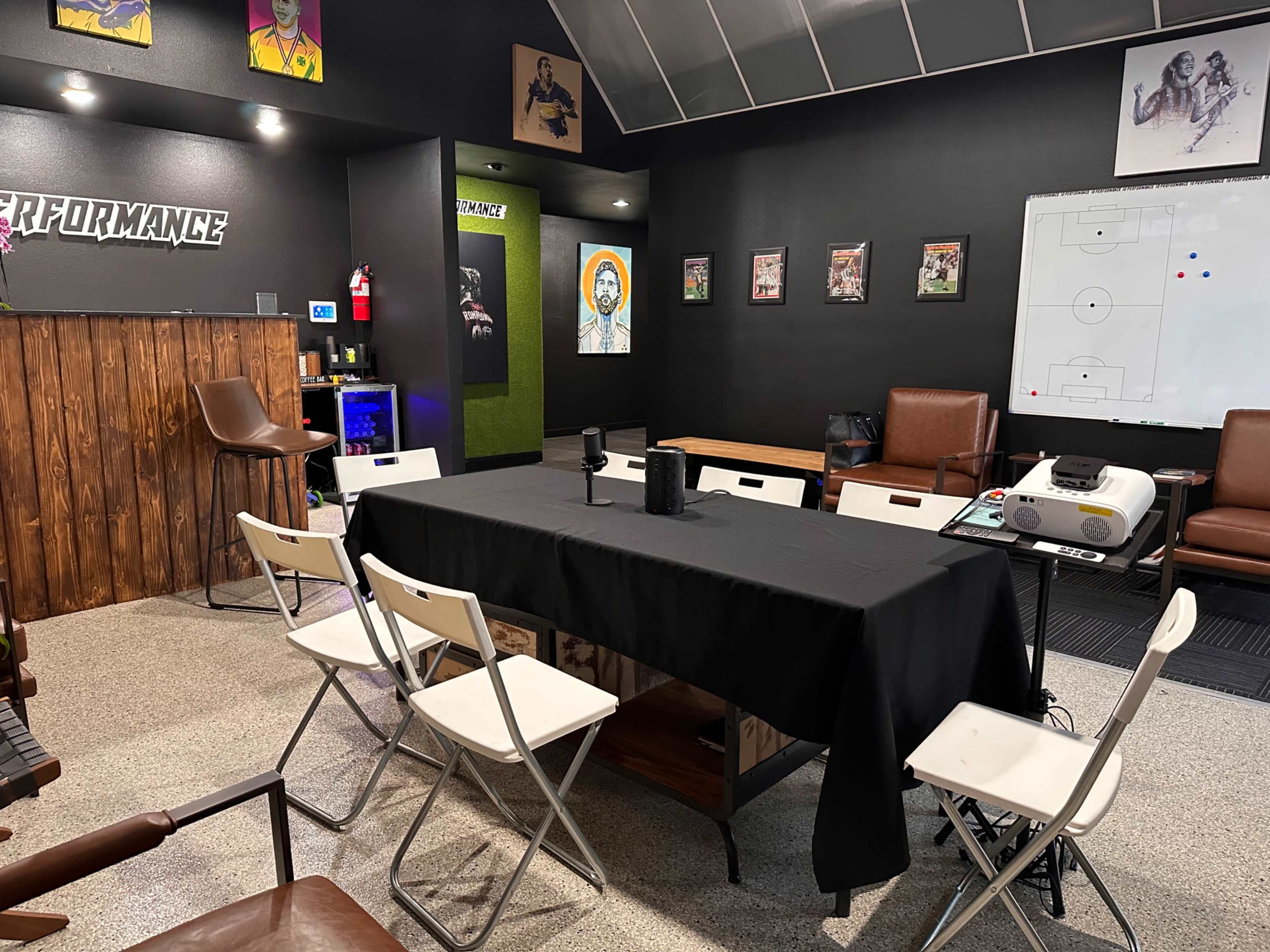 A modern meeting room with a black table surrounded by white folding chairs, featuring sports-themed decorations and a large whiteboard on the wall.