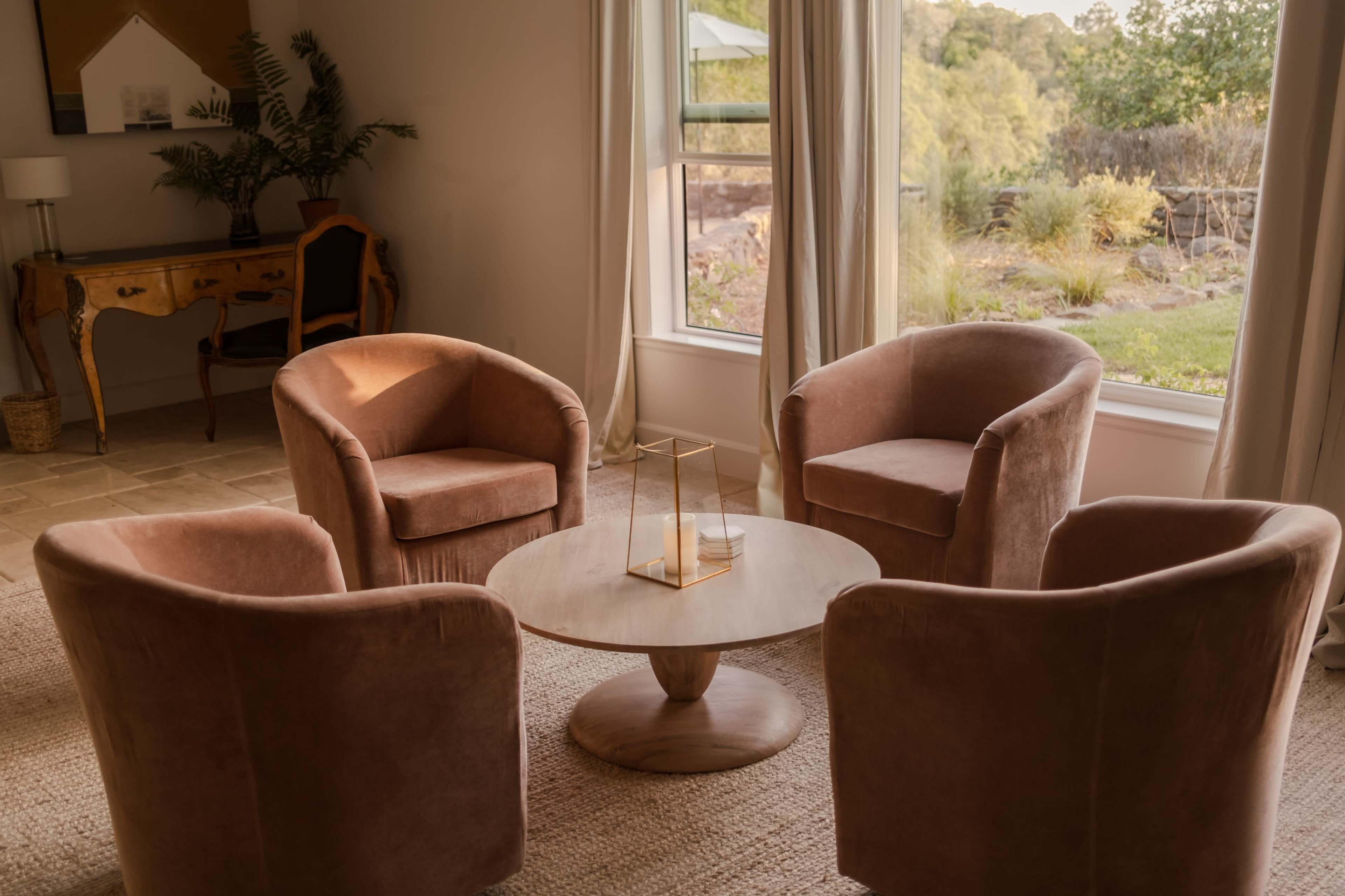 The image shows a cozy seating arrangement with four plush chairs surrounding a circular wooden coffee table in a well-lit living space.