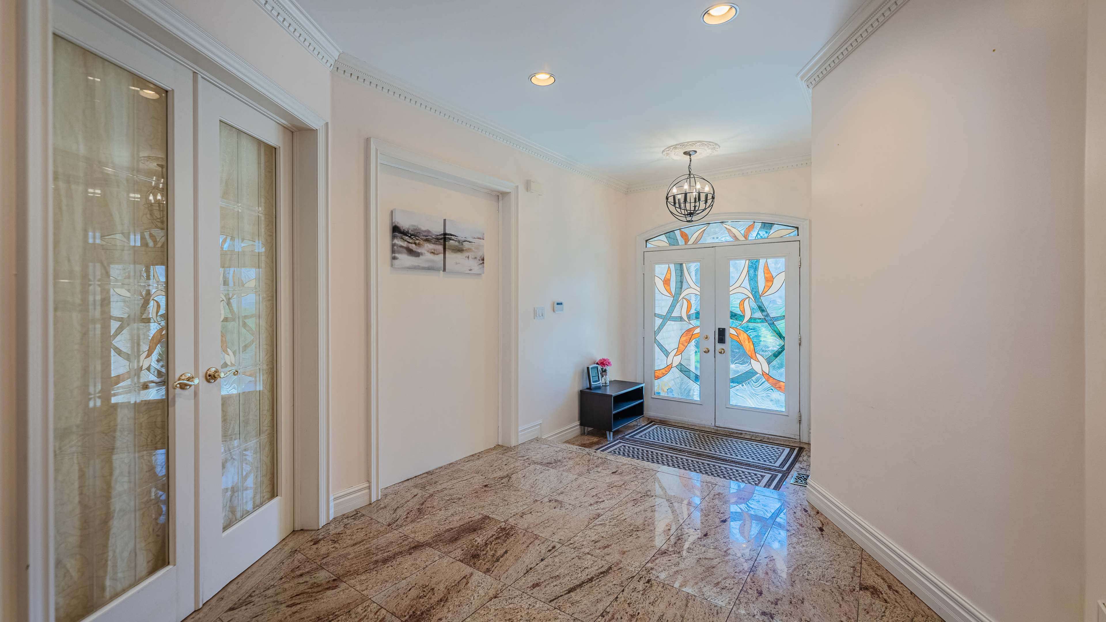 The image shows a spacious entryway with marble flooring, a decorative glass door featuring colorful designs, and a modern light fixture.