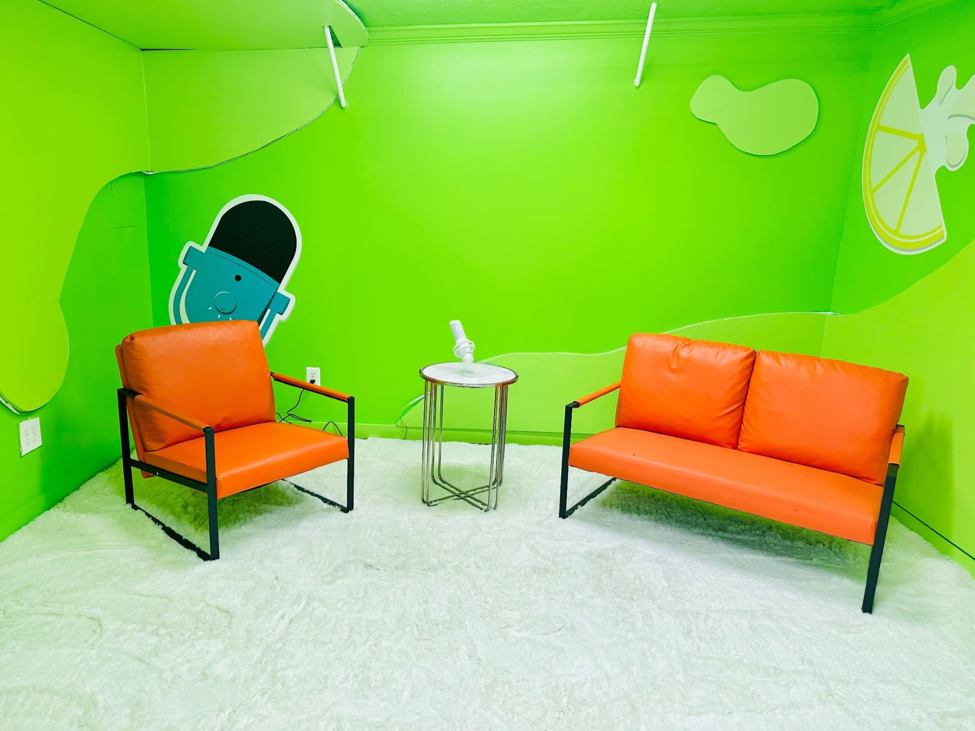 The image shows a small, brightly colored room with green walls, two orange sofas, and a round white table.