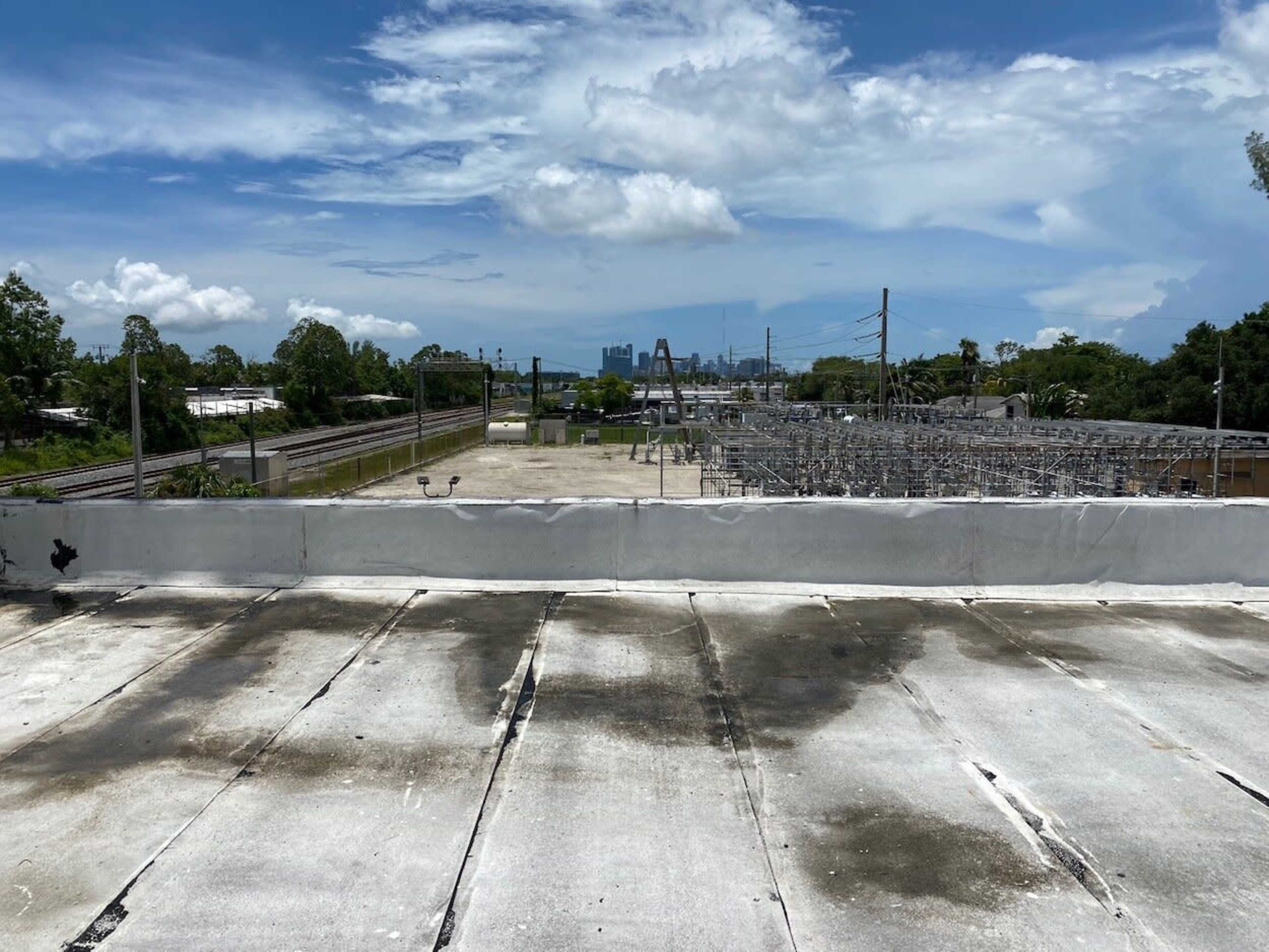 The image shows a flat rooftop with apparent stains, overlooking an electrical substation and railway tracks under a cloudy sky.