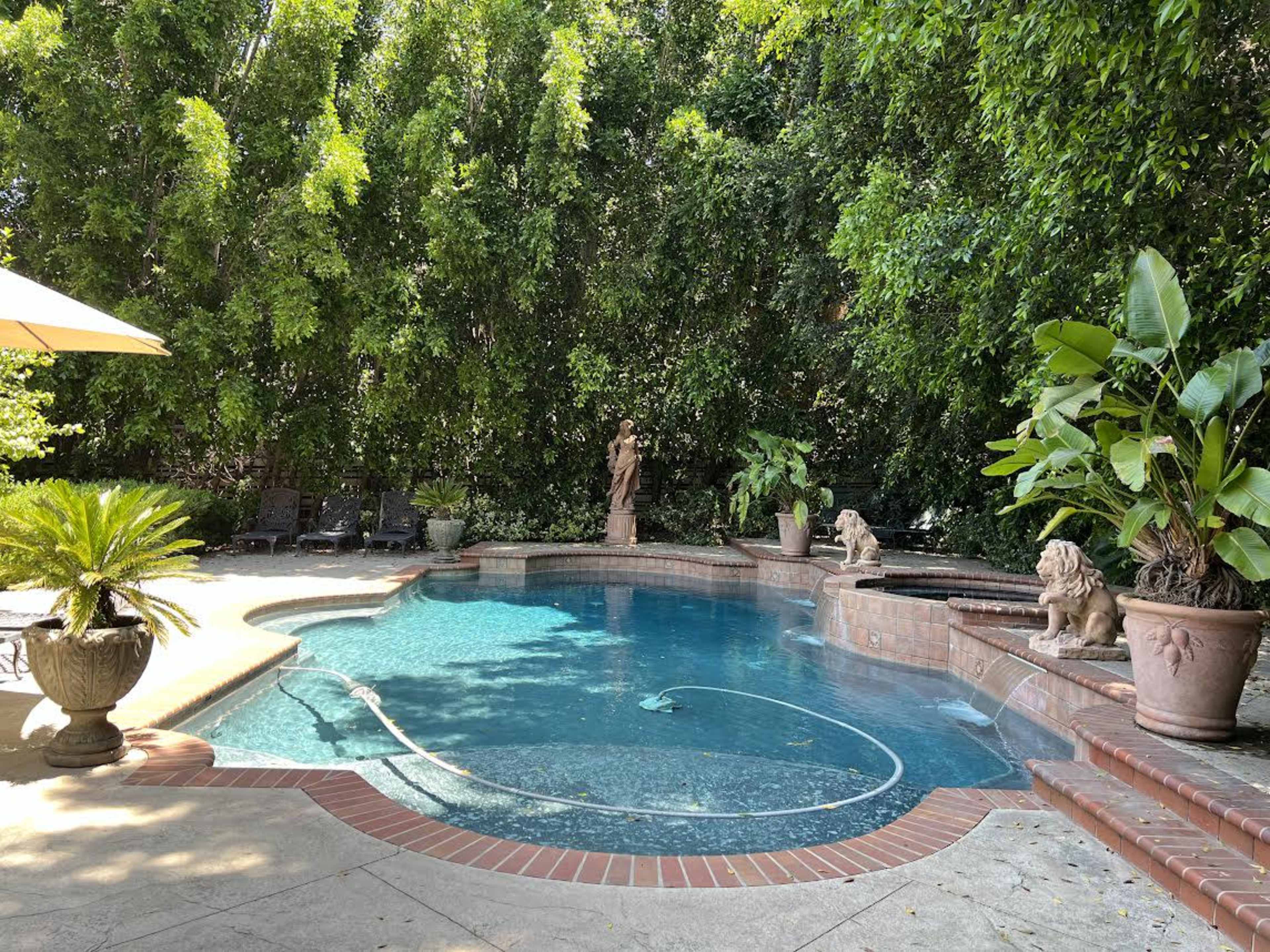 A swimming pool is surrounded by lush greenery and statues, with lounge chairs positioned nearby.