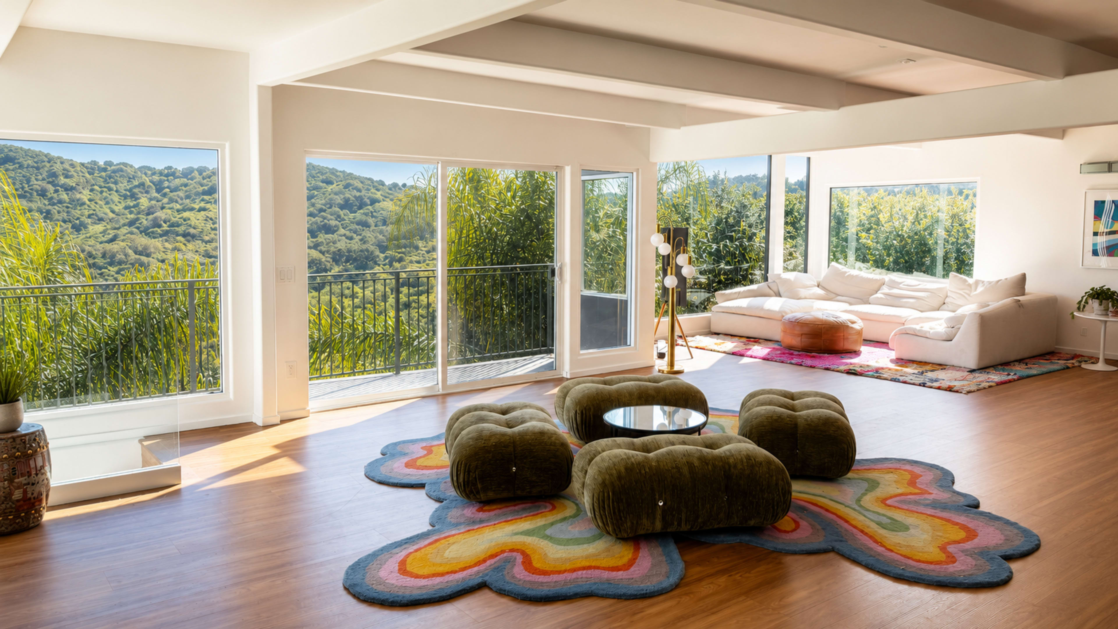 The image shows a spacious living room with large windows overlooking a green hillside, featuring a colorful area rug, modern furniture, and natural light.