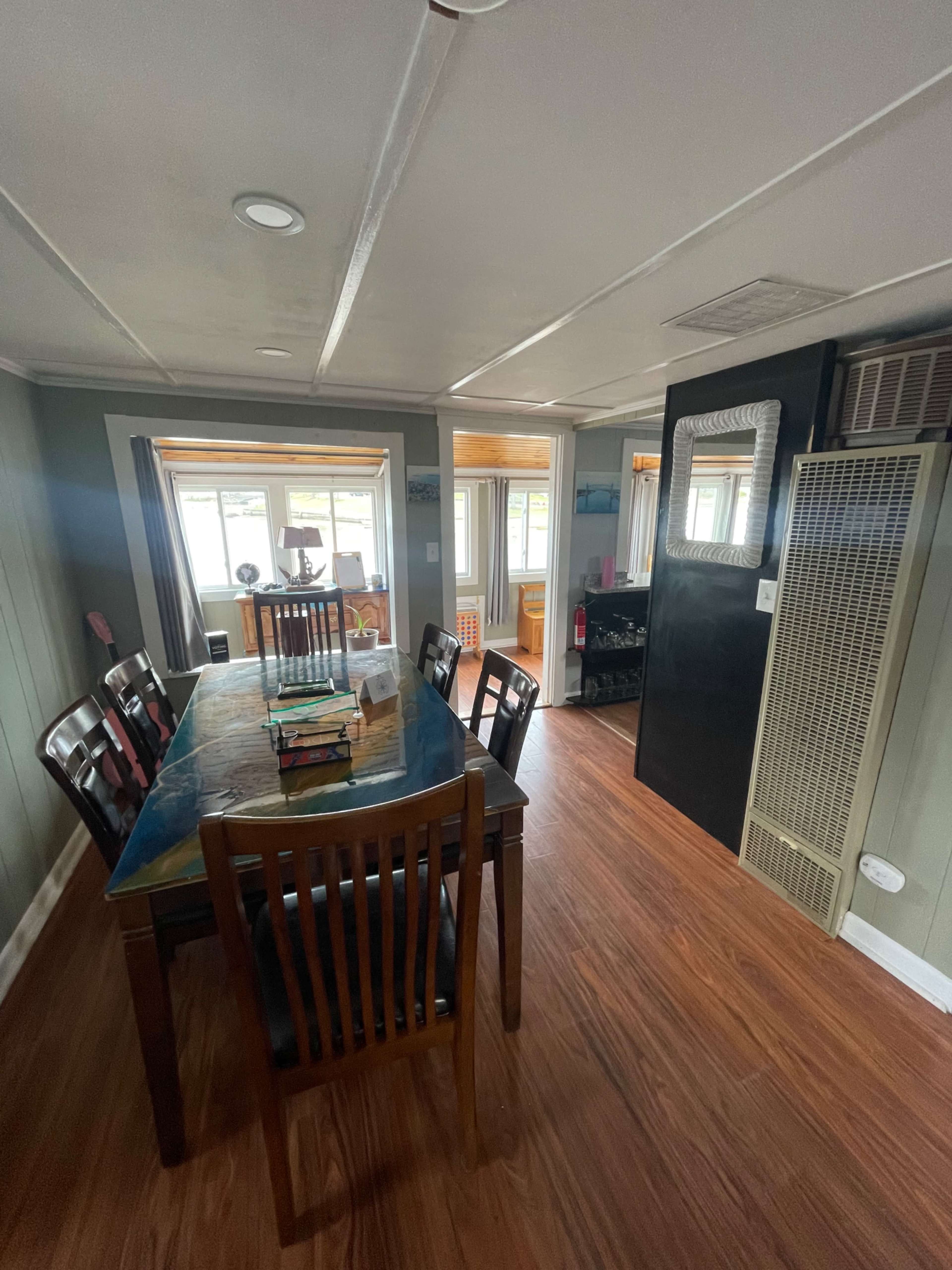 A dining area with a table and chairs, leading into a well-lit space featuring windows and a heater.