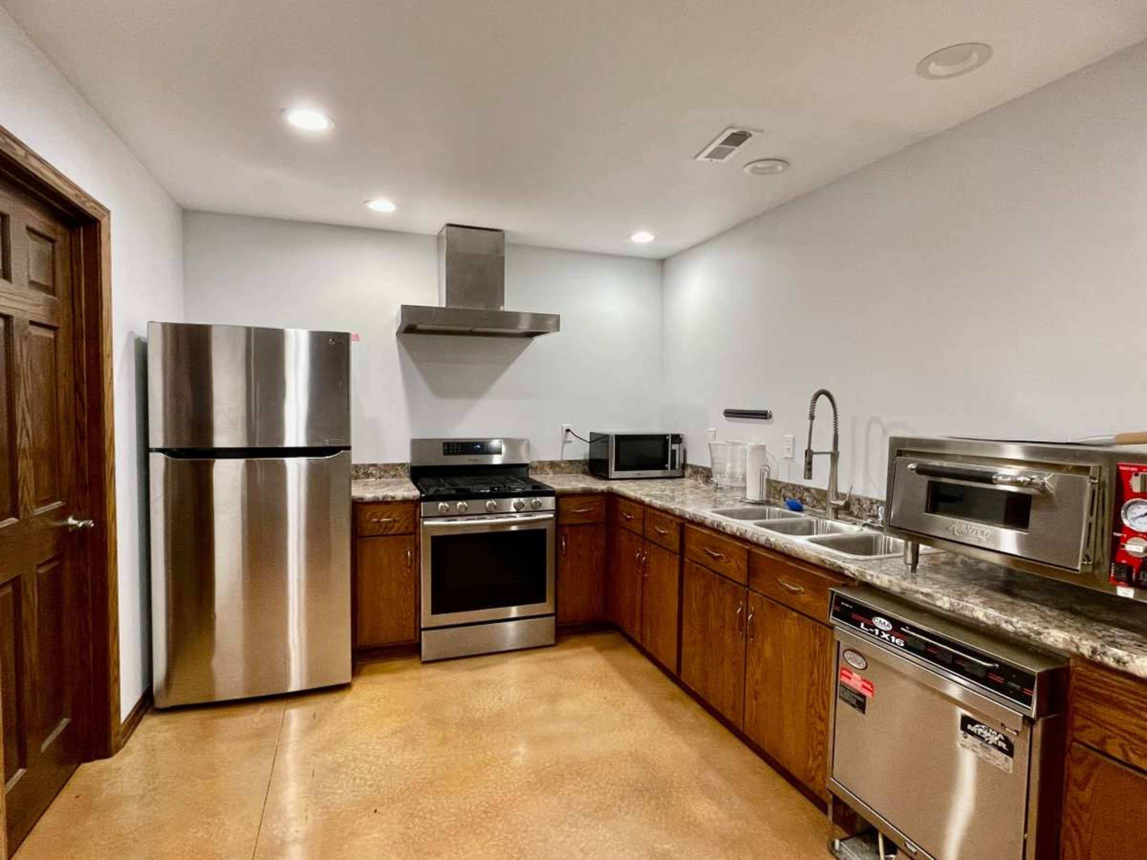 The image shows a modern kitchen with stainless steel appliances, including a refrigerator, oven, and microwave, complemented by wooden cabinets and a stainless steel sink.