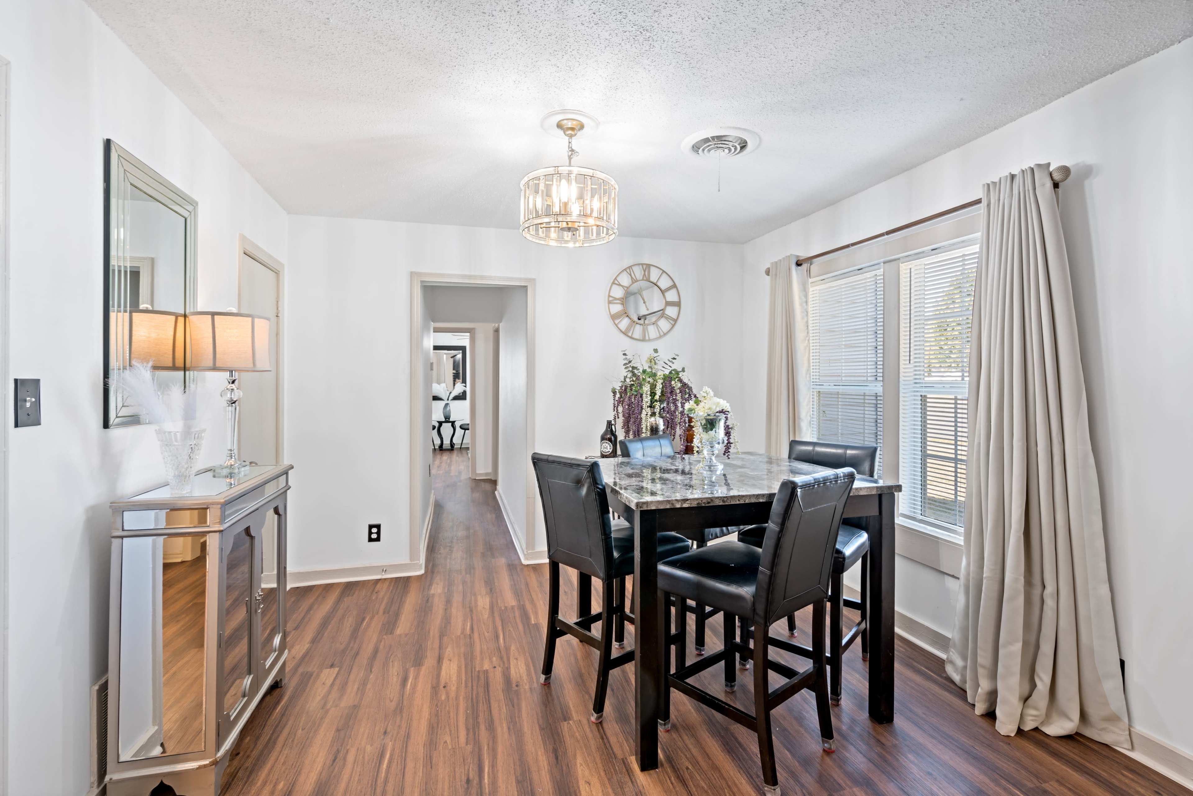 A dining area features a table with four black chairs, a chandelier overhead, and a mirror on the wall.