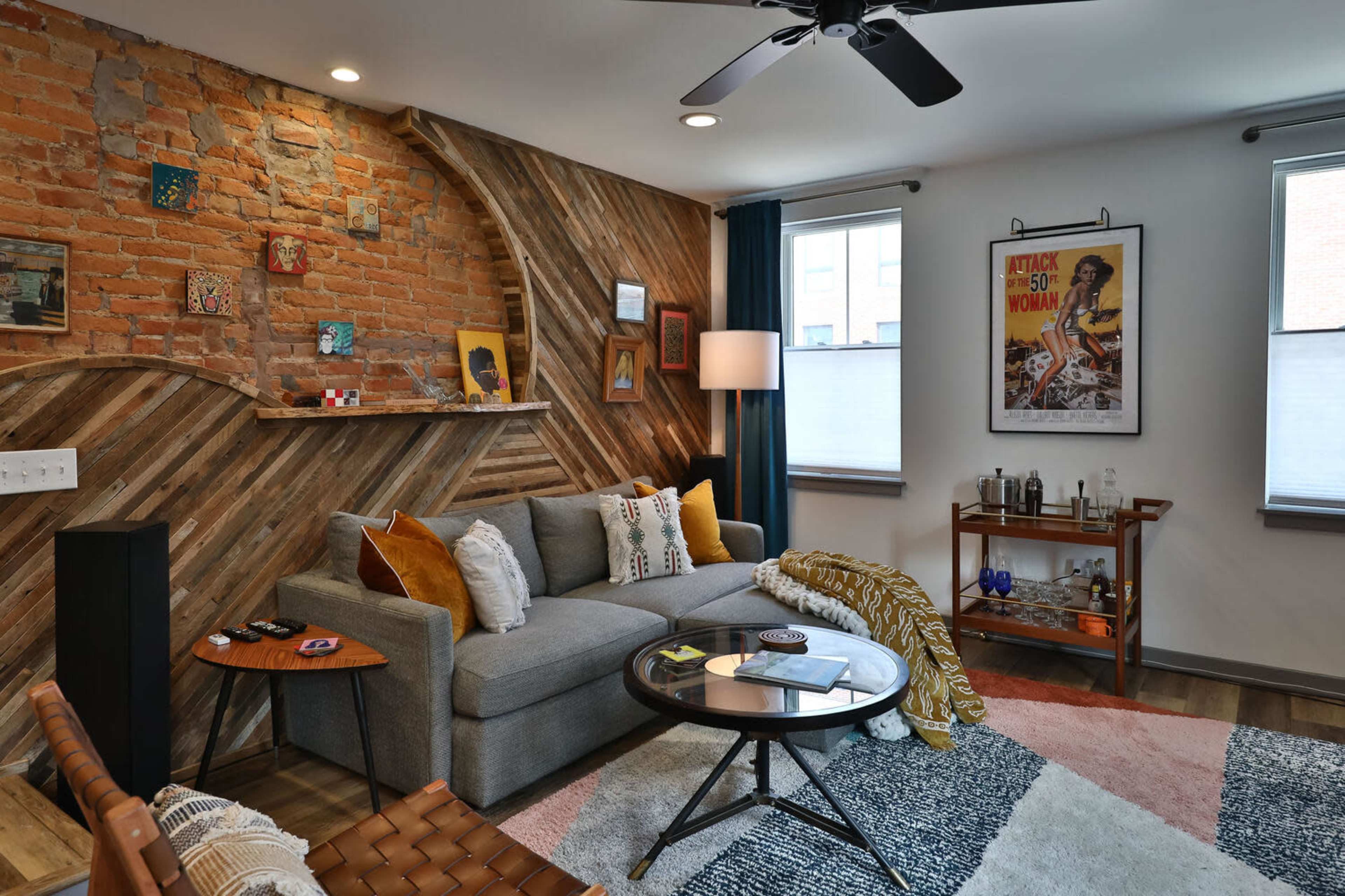 A modern living room with a mix of brick and wooden walls, featuring a gray sofa, a round coffee table, and decorative elements on the walls and shelves.