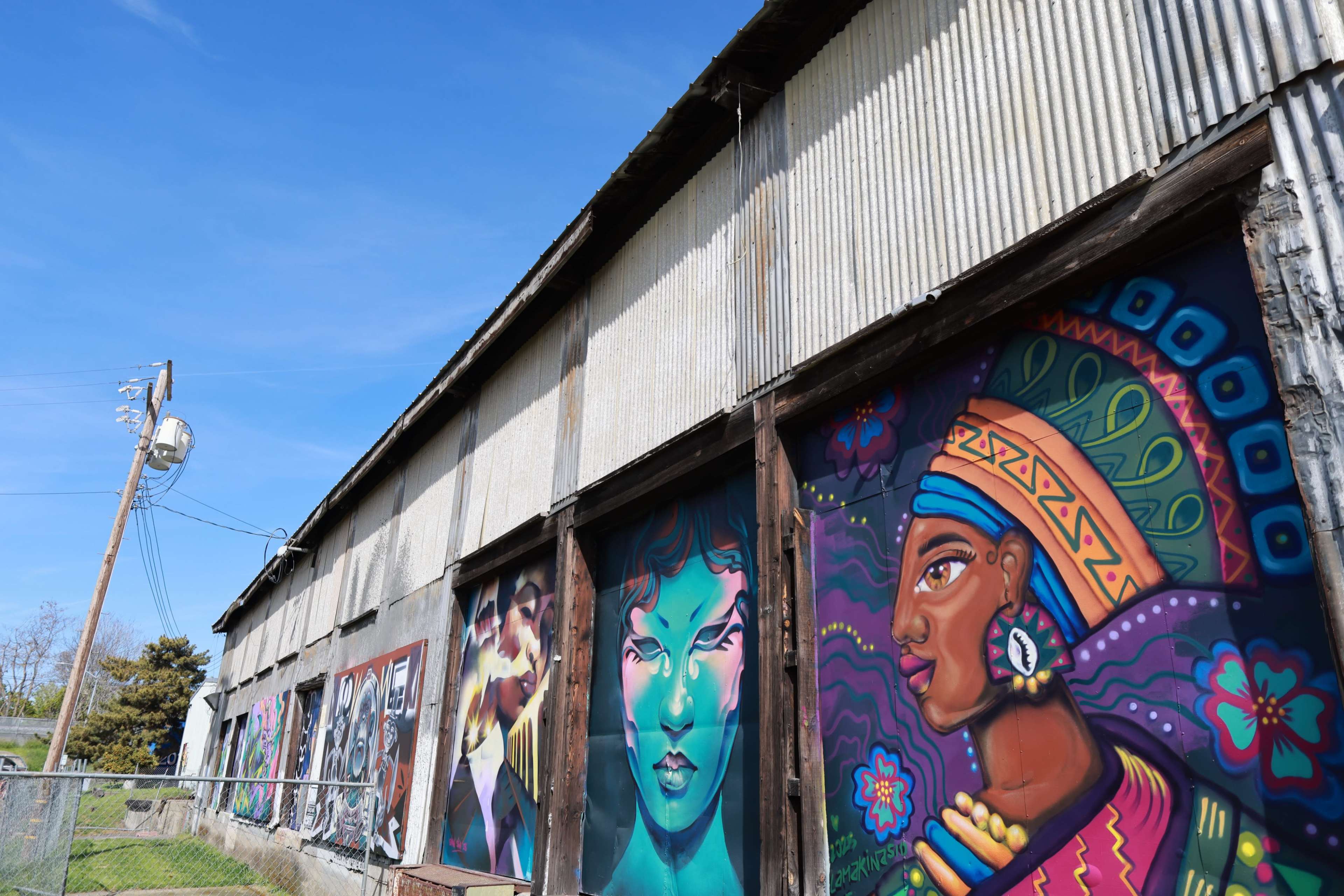 The image shows a weathered building with colorful murals depicting various faces and cultural themes along its exterior wall.