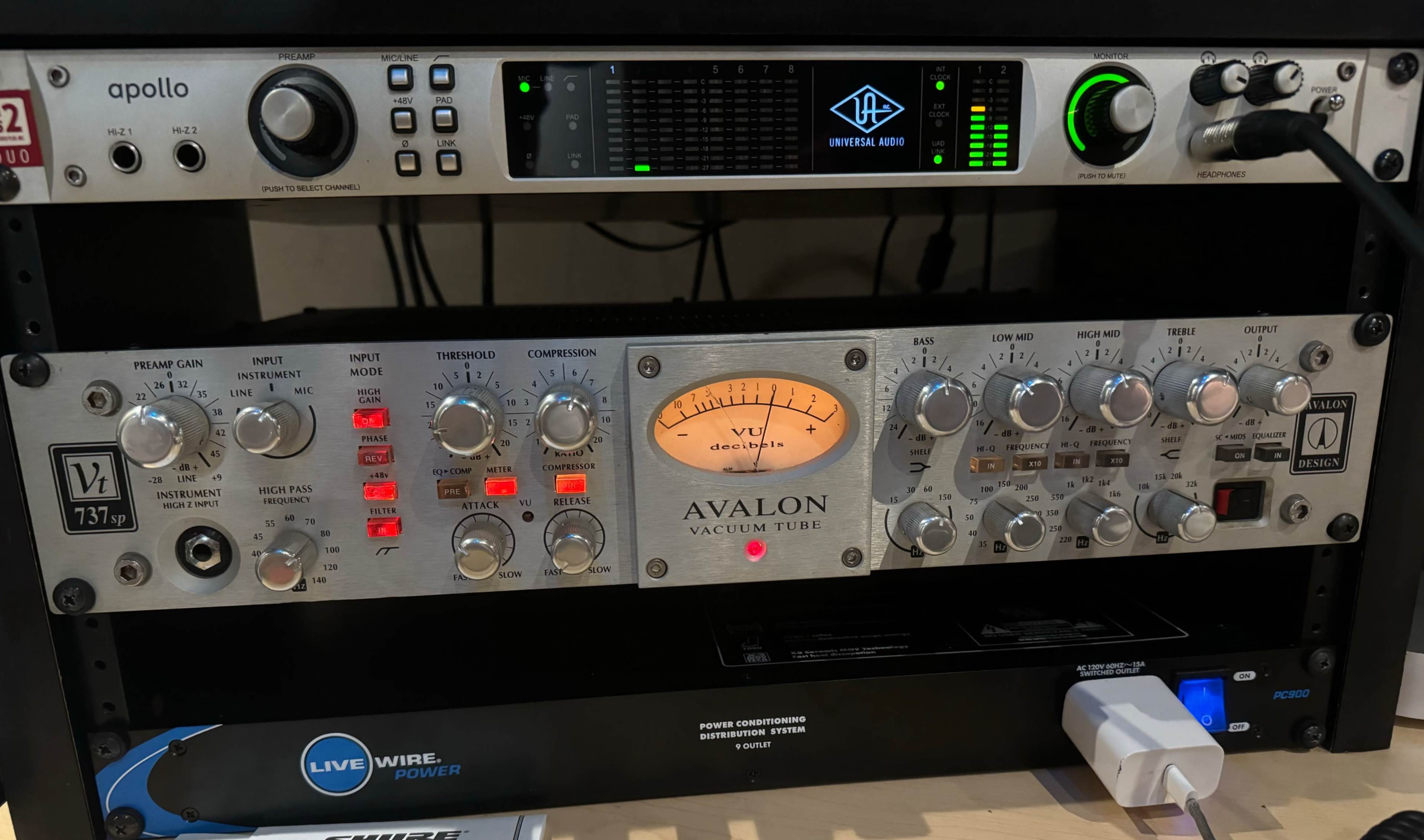 The image shows a rack-mounted audio equipment setup with an Avalon vacuum tube preamp at the center, flanked by a Universal Audio Apollo interface above and power distribution below.