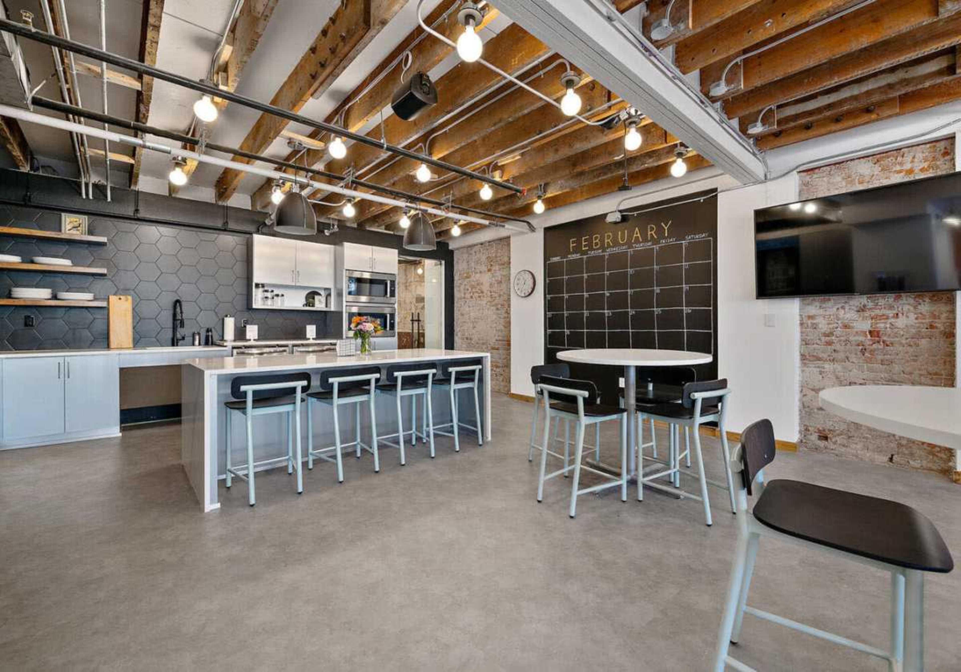 The image shows a modern kitchen space with exposed wooden beams, a large island, and bar seating, featuring a black hexagonal backsplash and minimalist decor.
