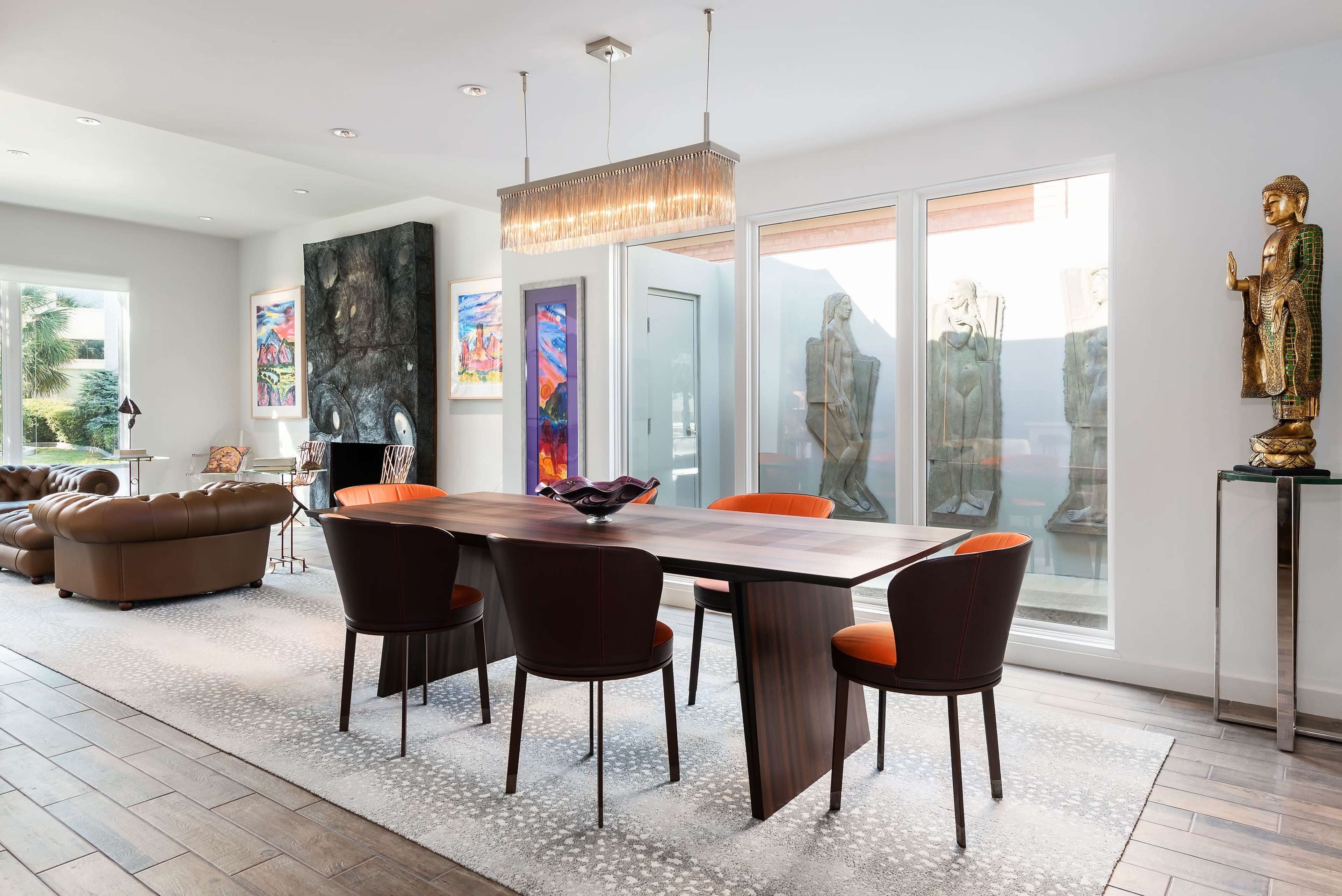 A modern dining area featuring a rectangular wooden table surrounded by four chairs, with a large window and various artworks displayed on the walls.