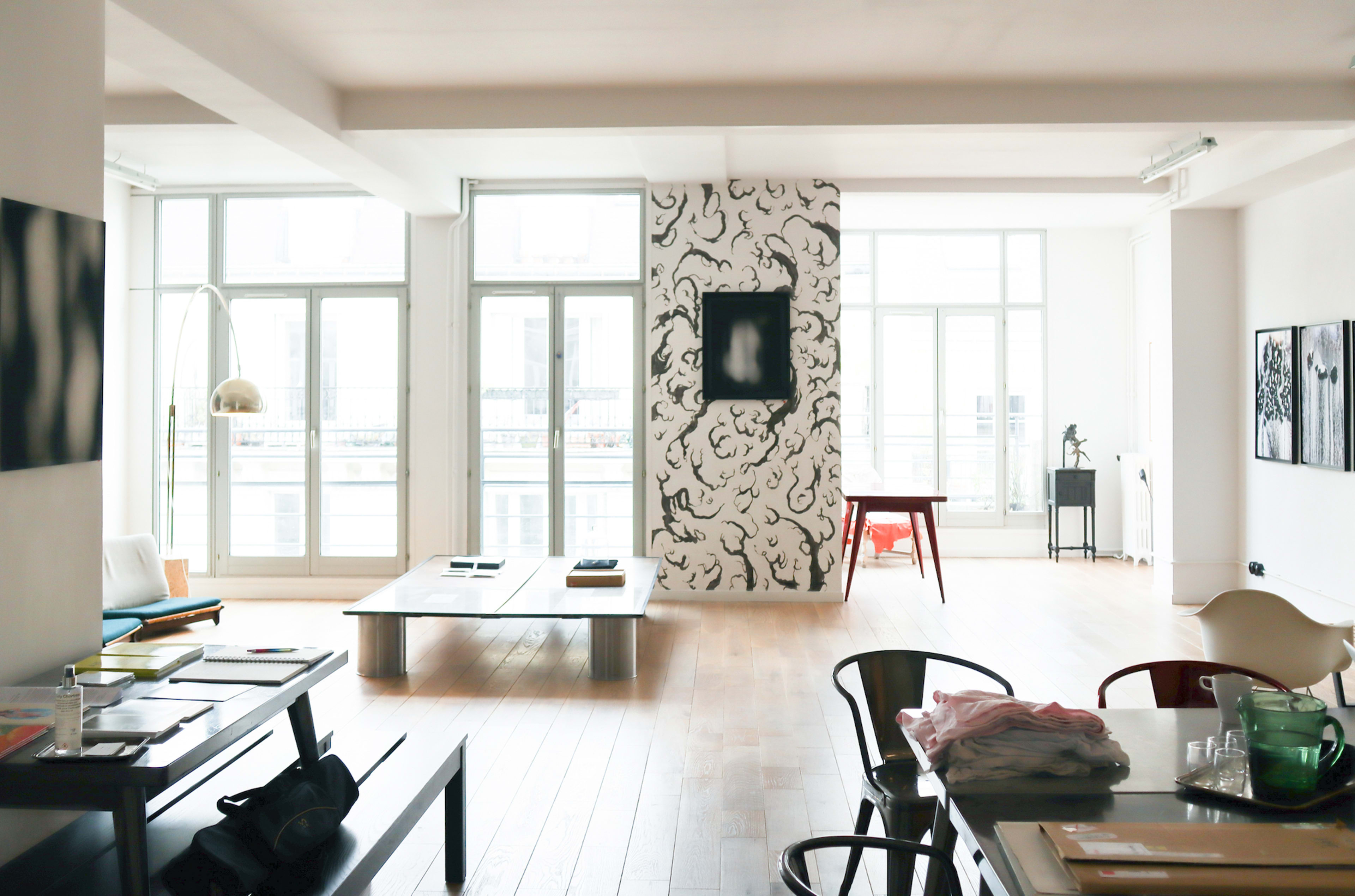 The room features a spacious, modern interior with large windows, hardwood floors, and a decorative wall pattern.