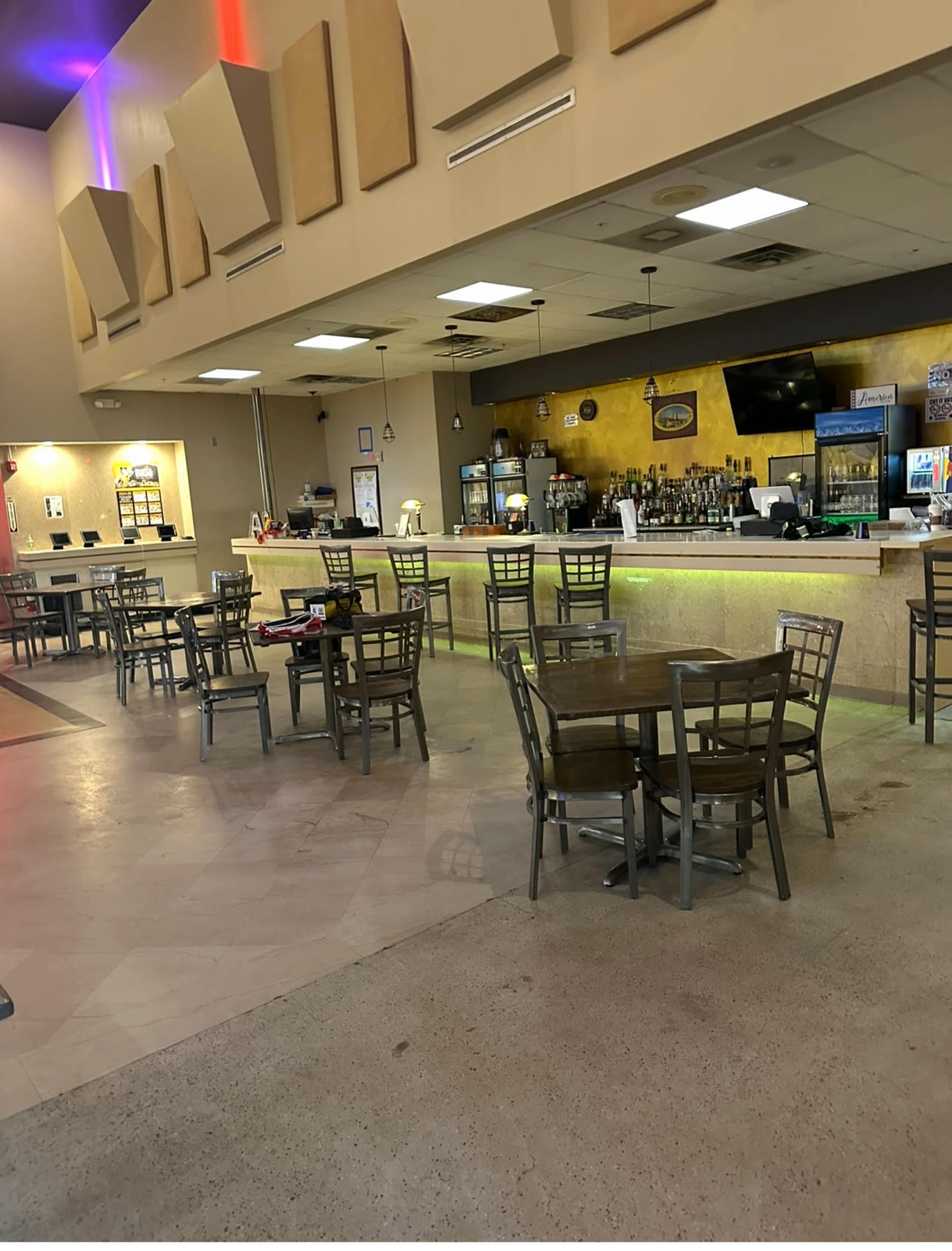 The image shows a spacious restaurant interior with empty tables and a bar area illuminated by colorful lights.