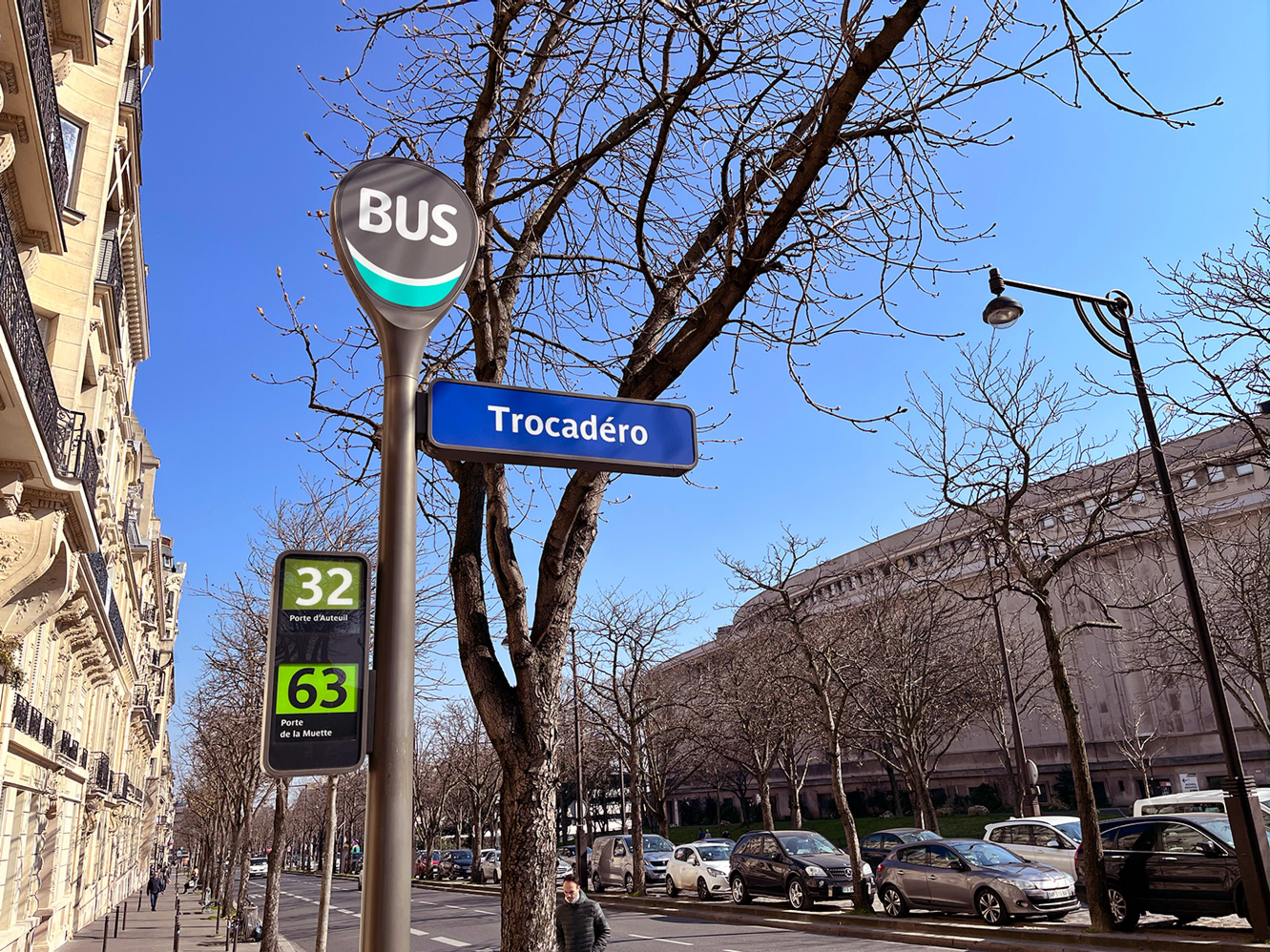 A street sign indicating the Trocadéro bus stop, located alongside a tree-lined avenue in bright daylight.