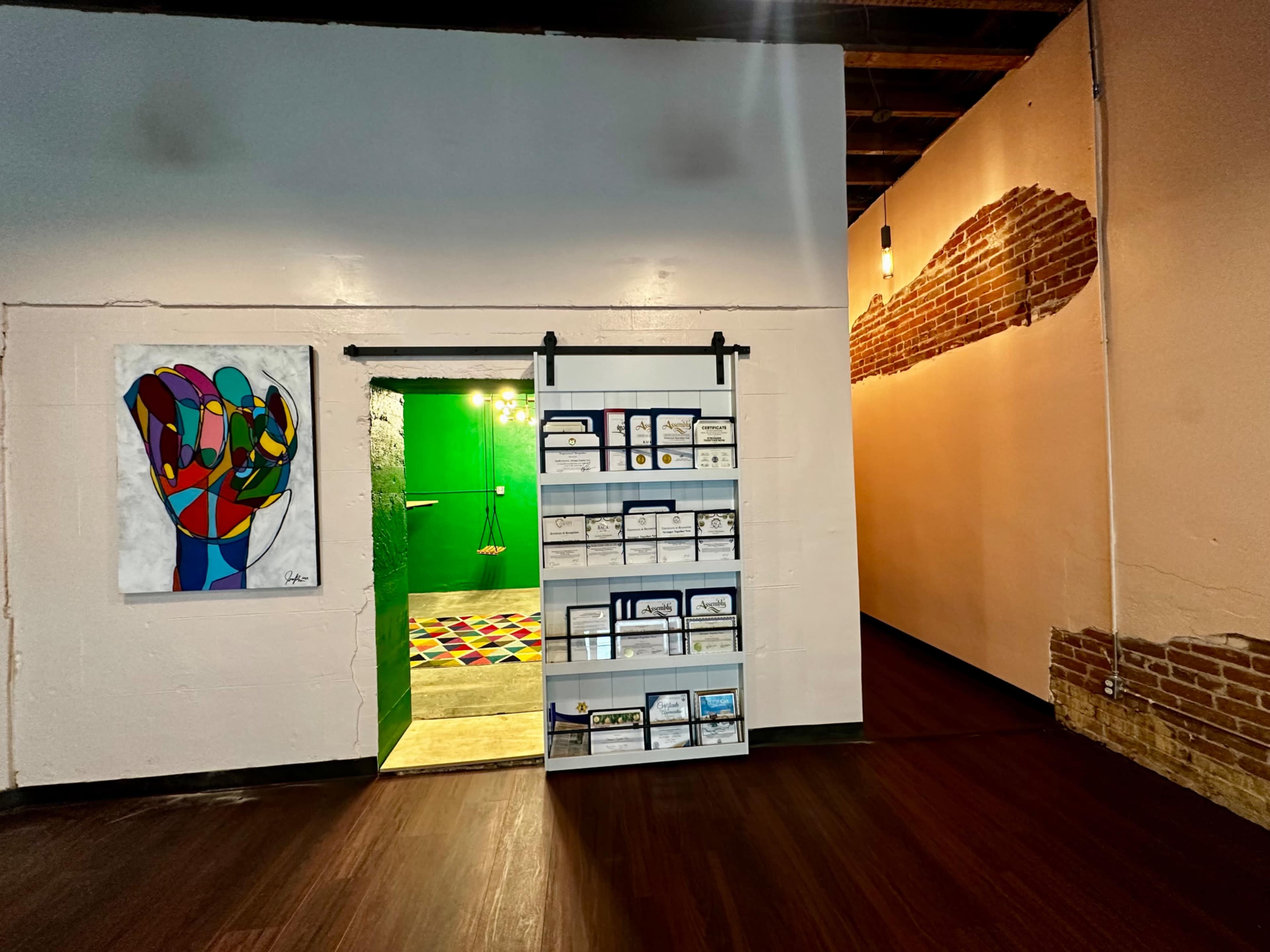 The image shows an interior space with a colorful mural of a raised fist on the left, a green door leading to another room, and a display rack with various brochures mounted on the wall.