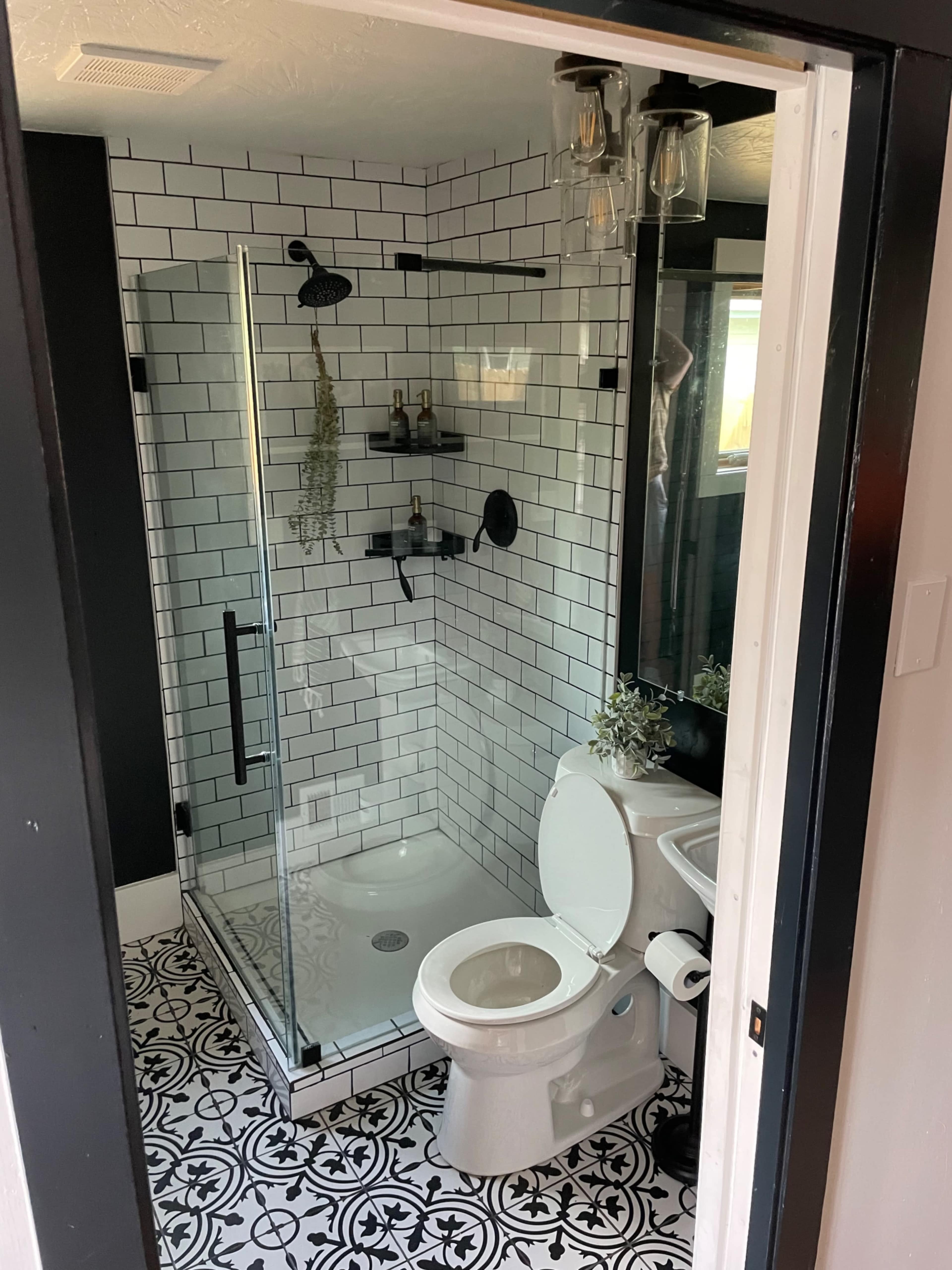 A modern bathroom featuring a glass-enclosed shower, a white toilet, and patterned black-and-white floor tiles.